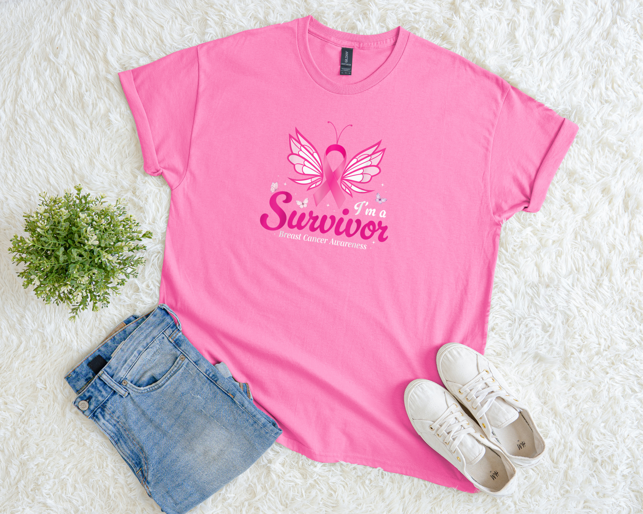 Pink t-shirt with 'I'm a Survivor' and butterfly design on a white surface with jeans and sneakers.