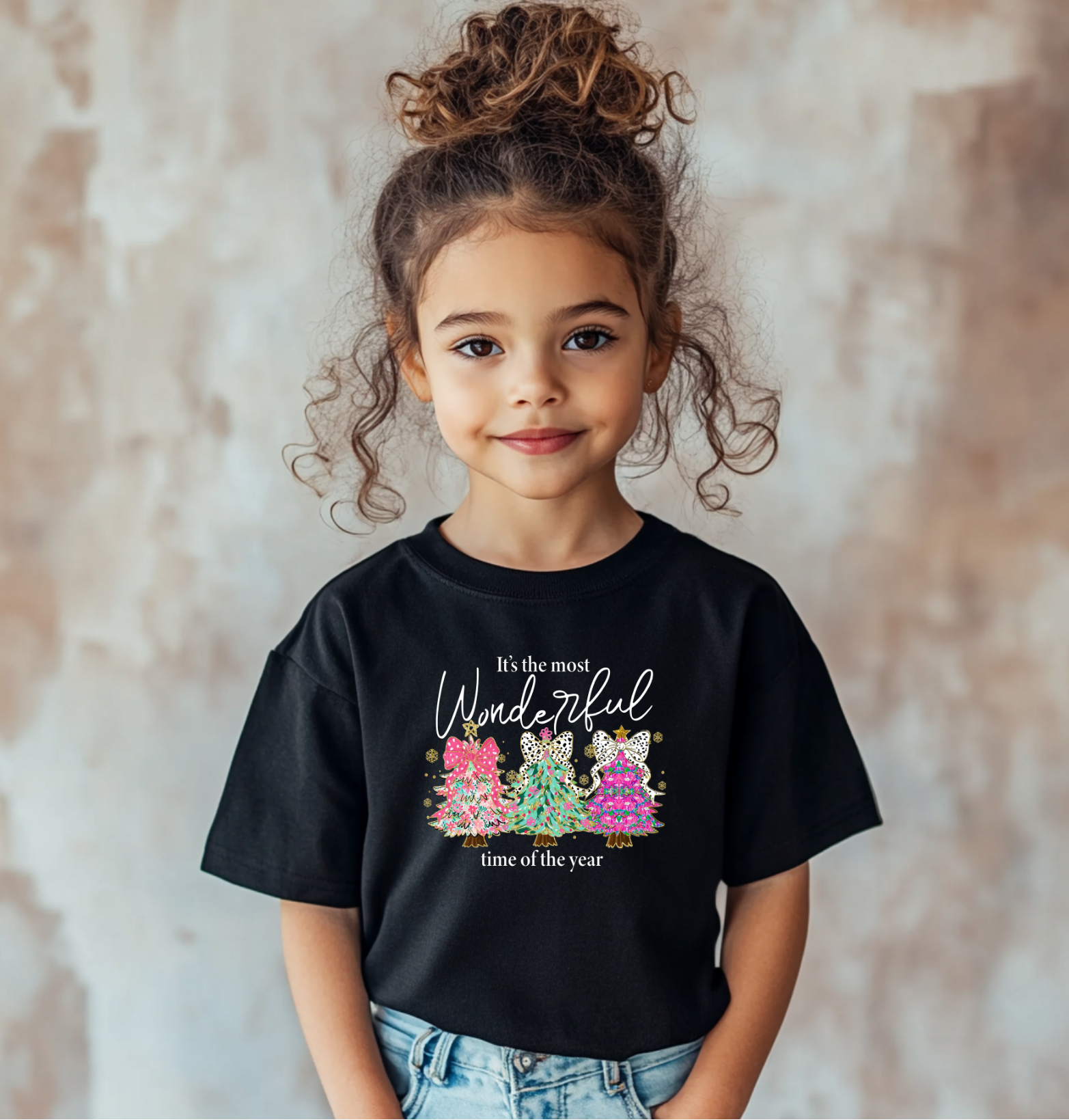 Christmas t-shirt with colorful trees and leopard bows that reads “It’s the Most Wonderful Time of the Year,” sitting happily near a decorated Christmas tree with presents.