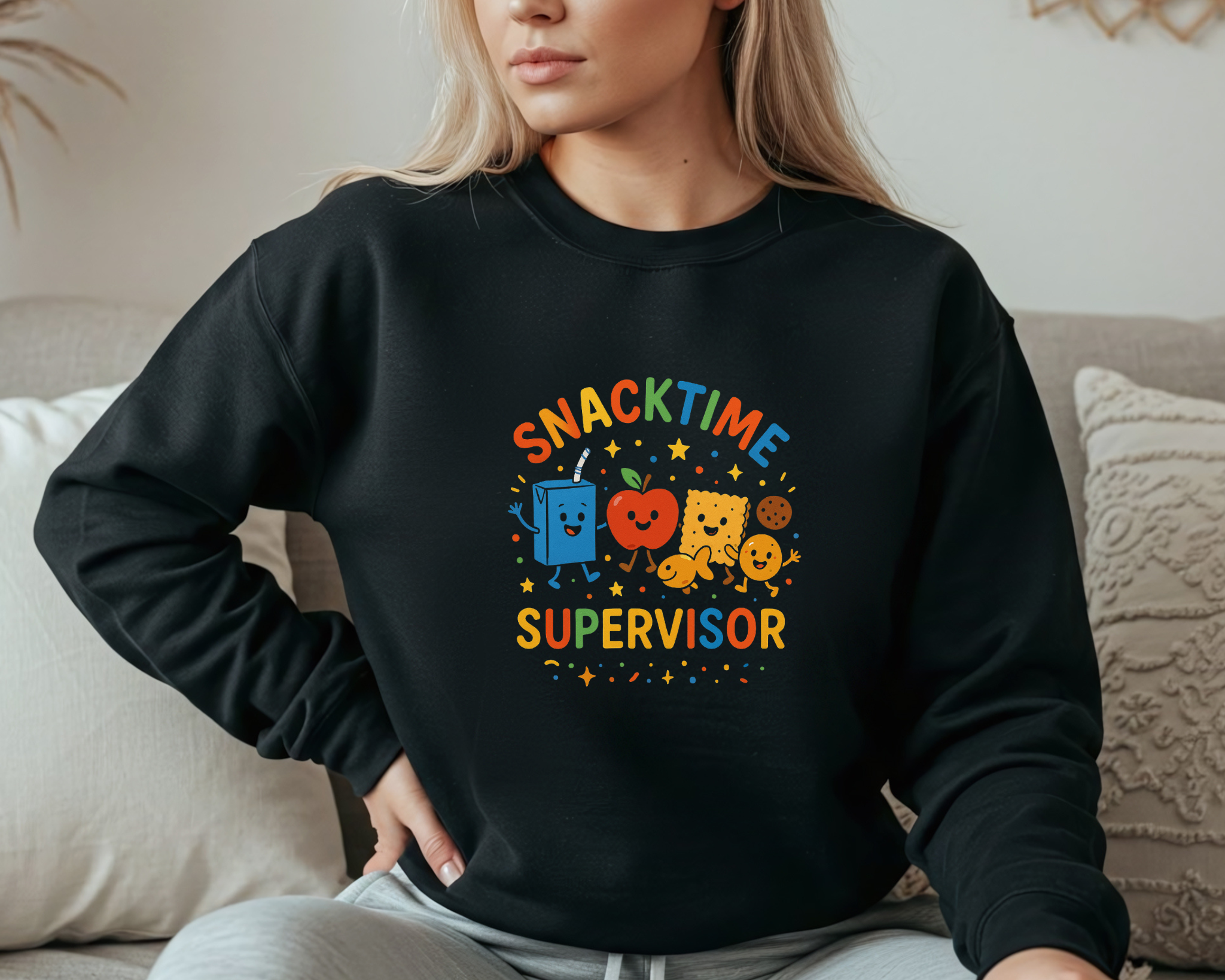 Black crewneck sweatshirt with “Snacktime Supervisor” in colorful text and smiling snack characters — juice box, apple, cracker, and cookie.