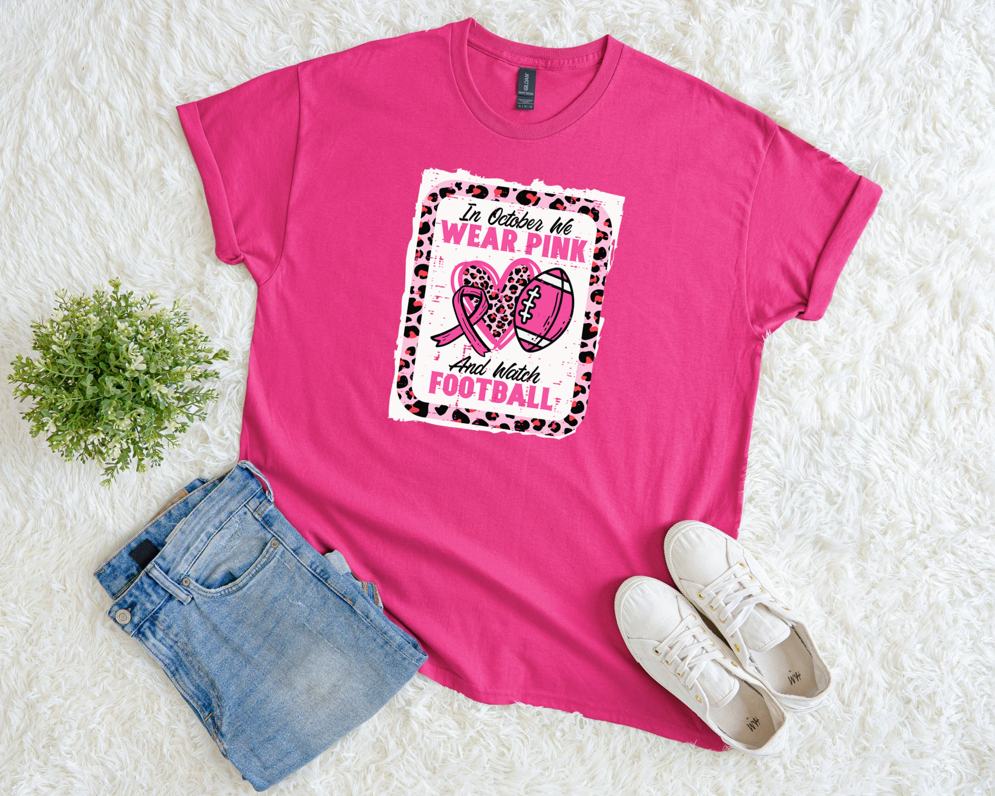 Bright pink breast cancer awareness t-shirt with a leopard print border, football and pink ribbon design, and the phrase “In October We Wear Pink and Watch Football.”