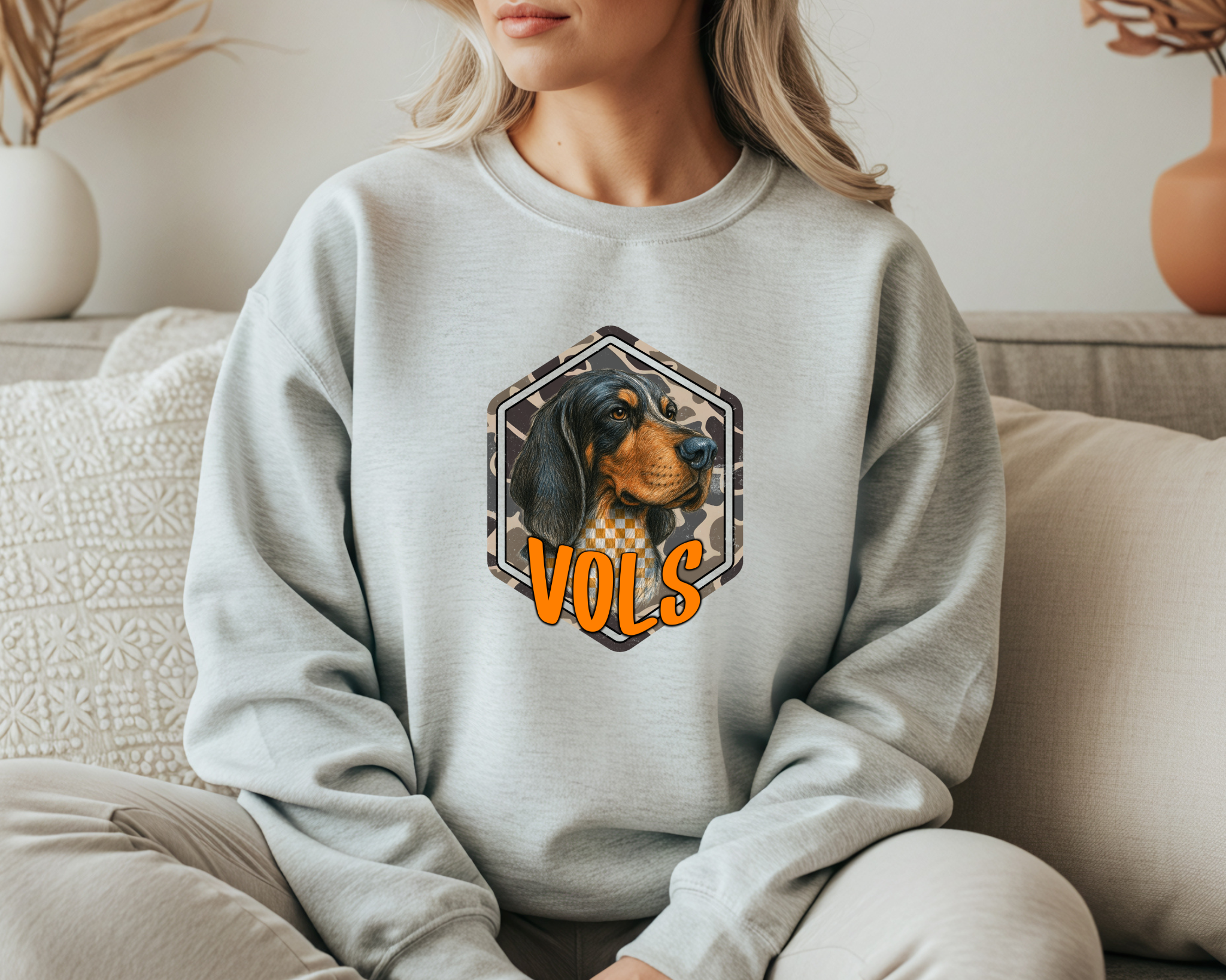 Person wearing a light gray sweatshirt with a dog graphic and 'VOLS' text, sitting on a couch.