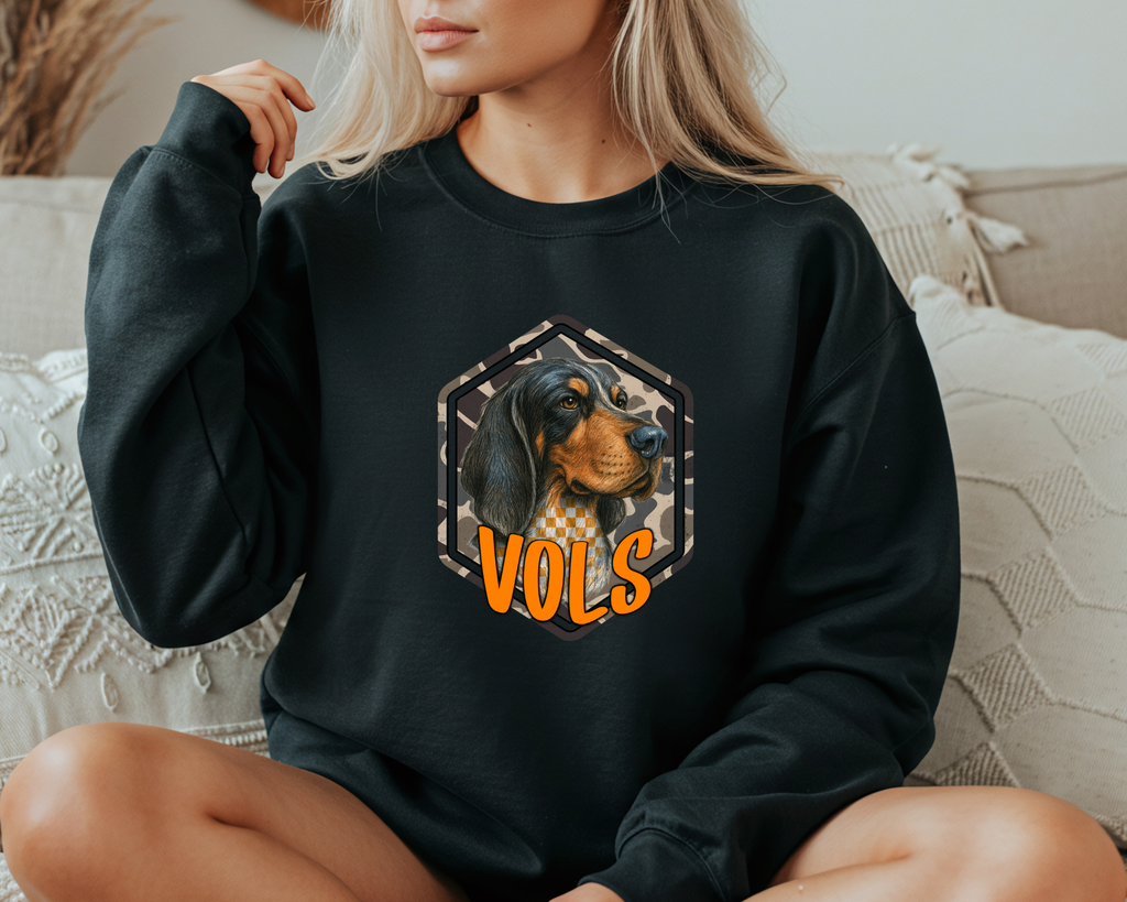 Person wearing a black sweatshirt with a dog graphic and 'VOLS' text on a couch.