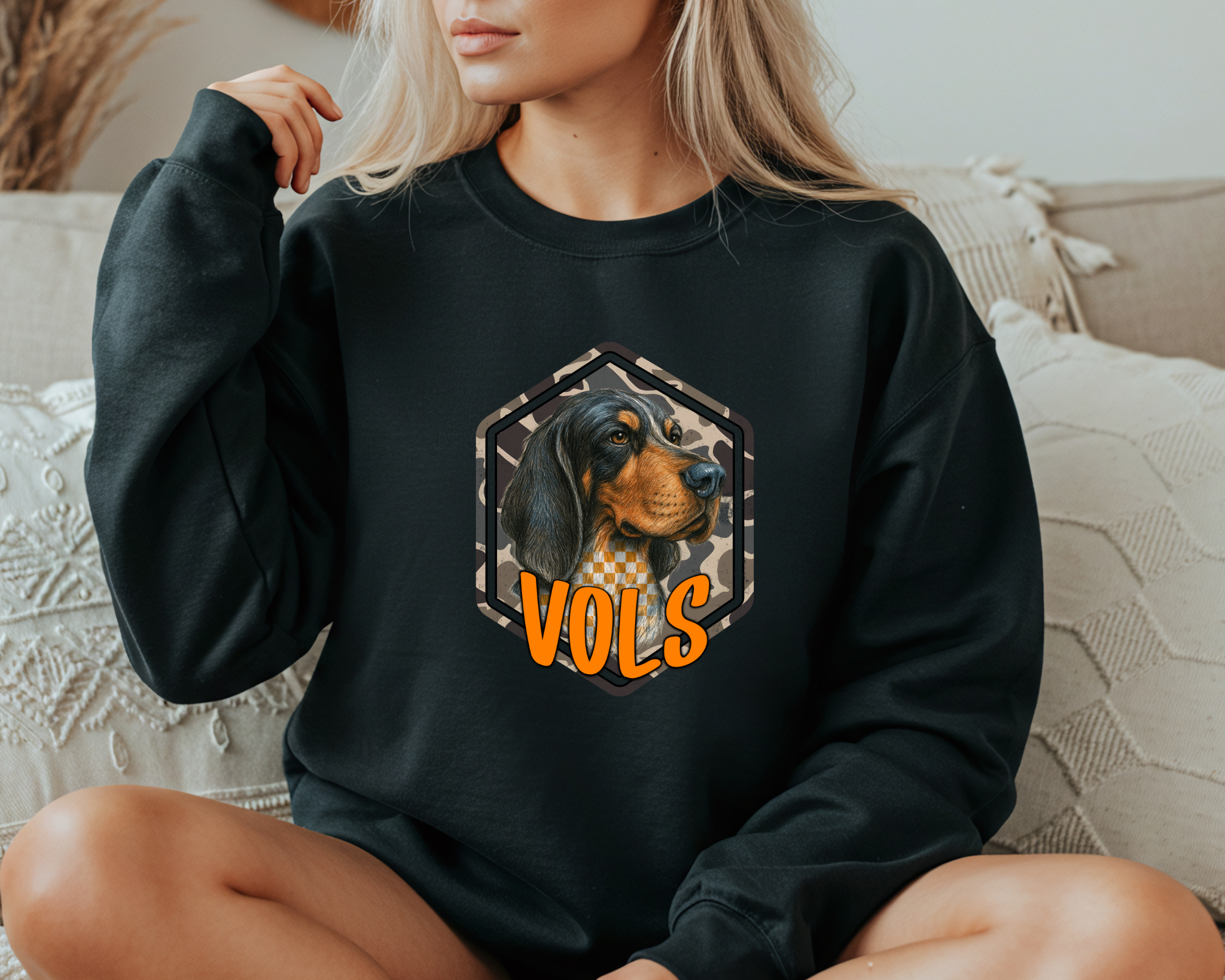 Person wearing a black sweatshirt with a dog graphic and 'VOLS' text on a couch.