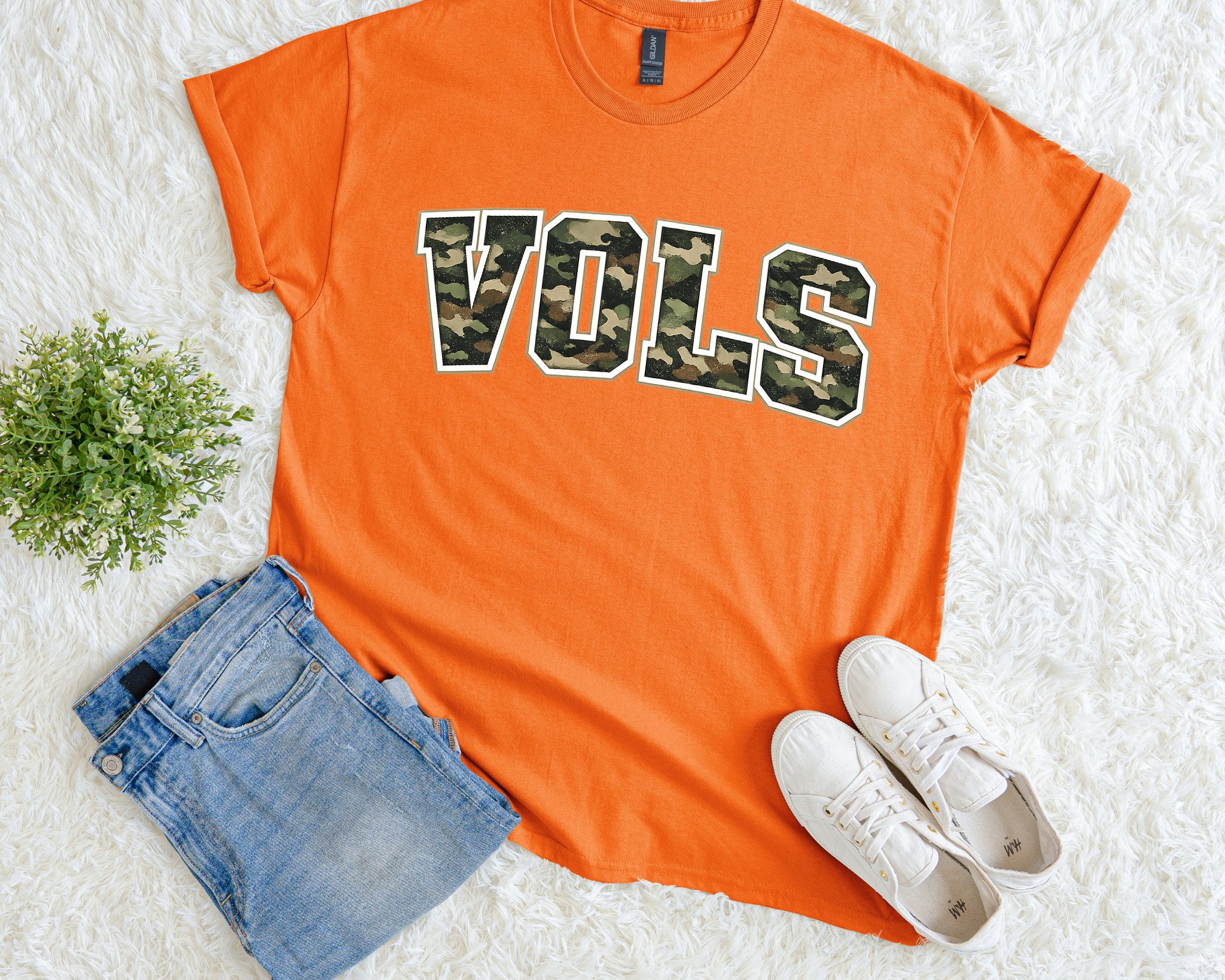 Orange t-shirt with 'VOLS' print, paired with denim shorts and white sneakers on a light background.