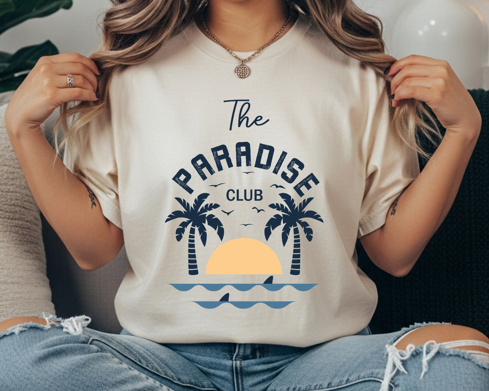 Comfort Colors t-shirt with “The Paradise Club” text and a retro beach graphic featuring palm trees, sunset, and waves in navy and light blue.