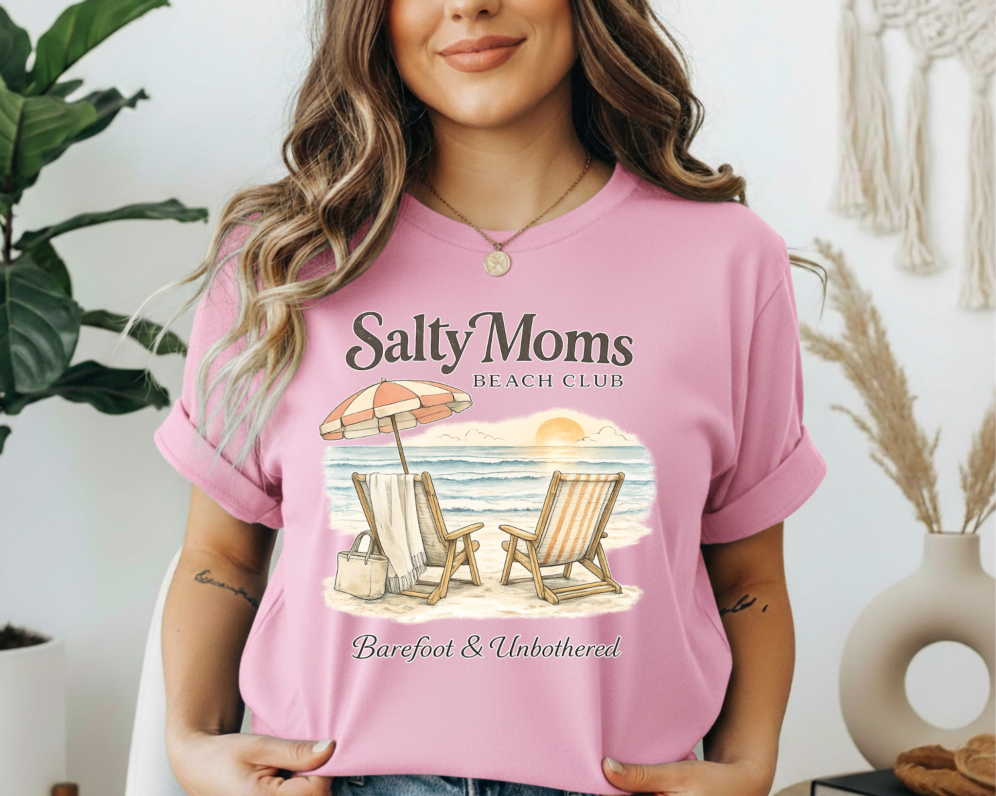 Woman wearing a pink t-shirt with 'Salty Moms Beach Club' design, standing indoors.