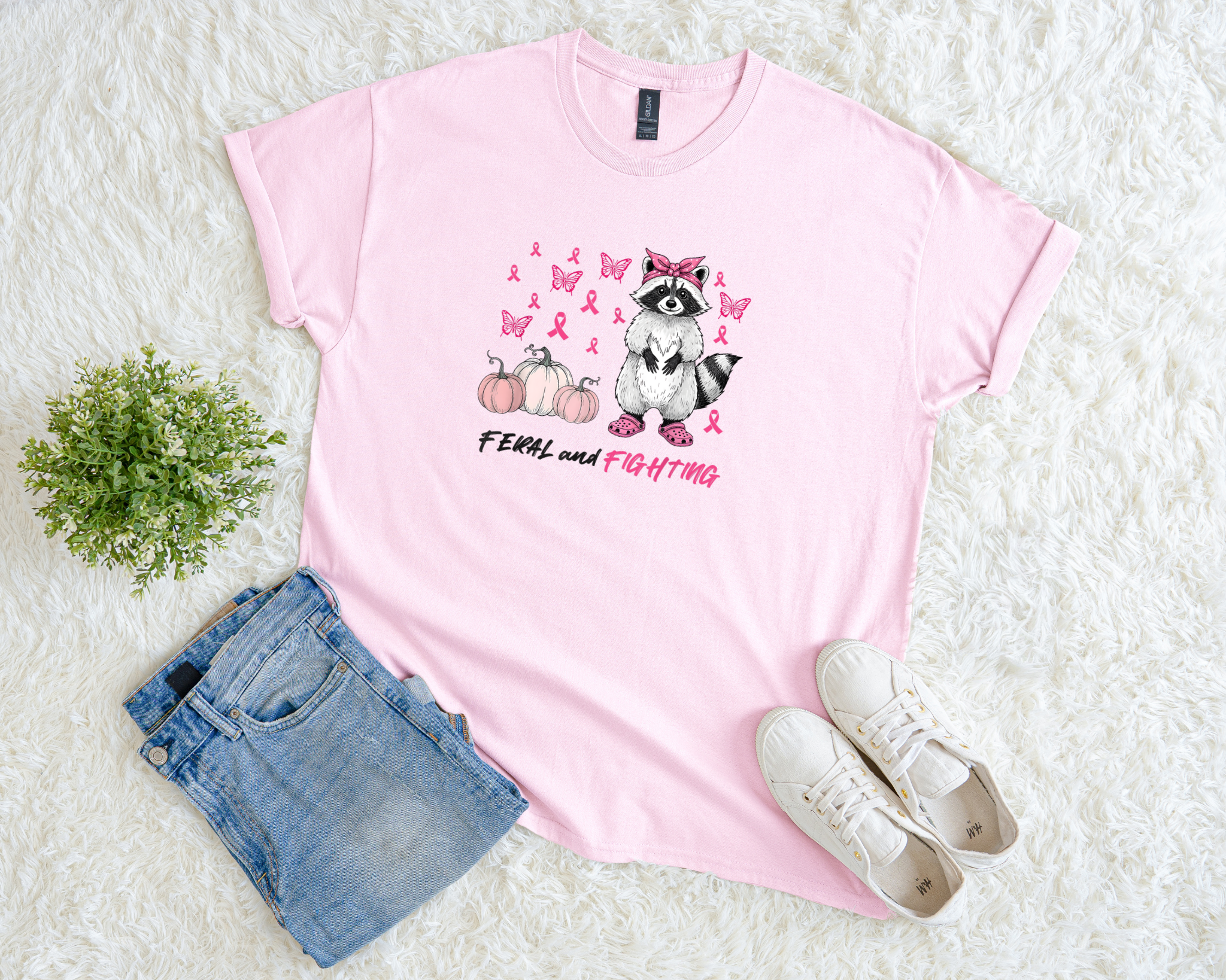 Pink t-shirt with a raccoon graphic and text, paired with denim shorts and white sneakers on a light background.
