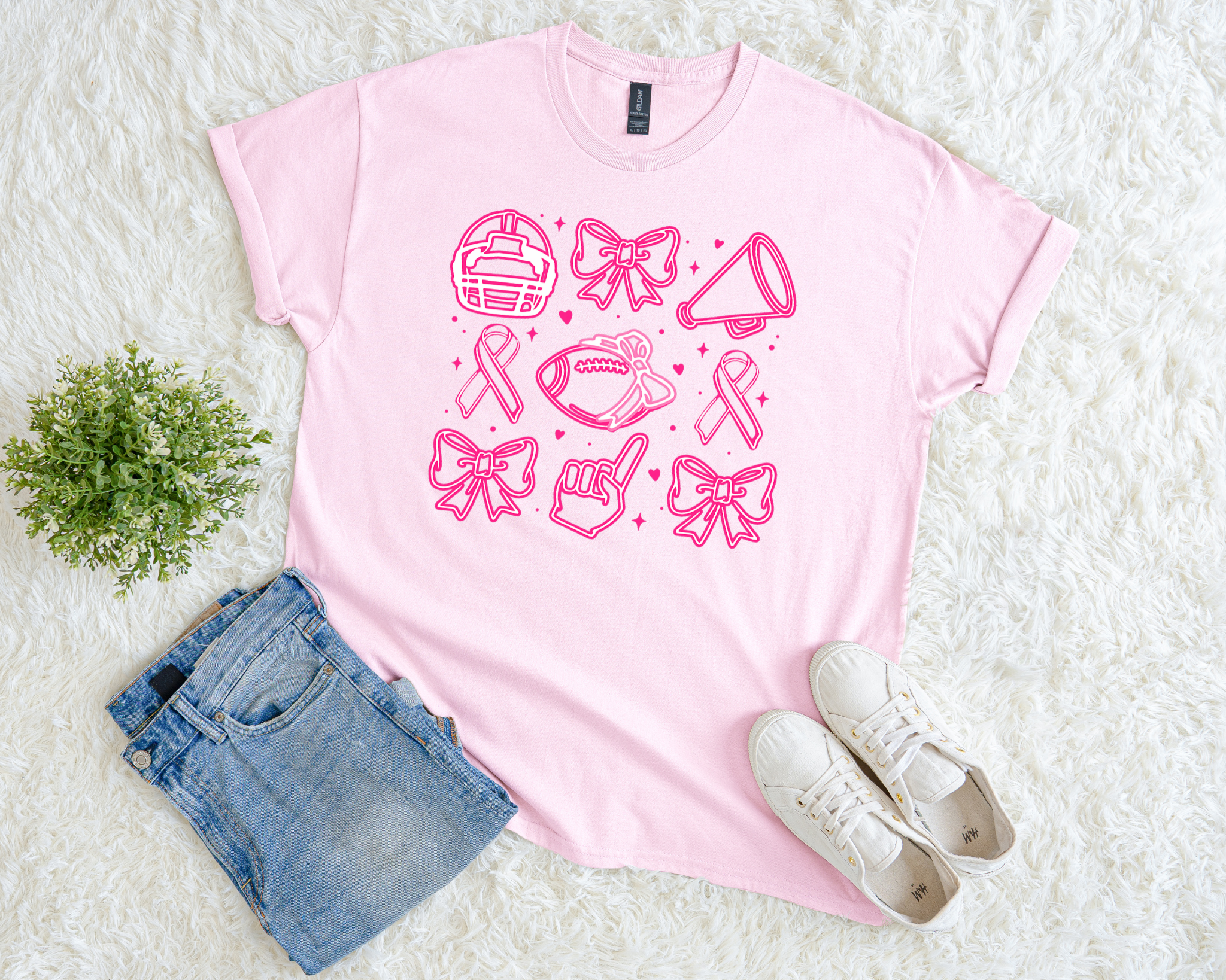 Light pink breast cancer awareness t-shirt with football helmet, ribbons, bows, foam finger, megaphone, and football graphic icons.