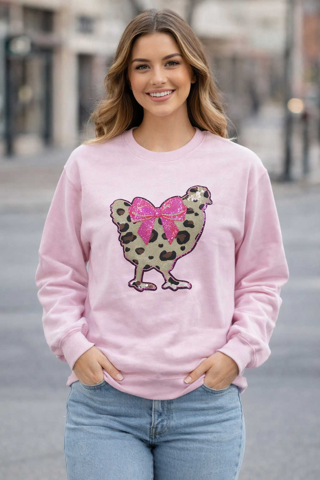 Light pink crewneck sweatshirt featuring an oversized sparkly sequin chicken in cheetah print with a hot pink bow, bold and playful graphic design.
