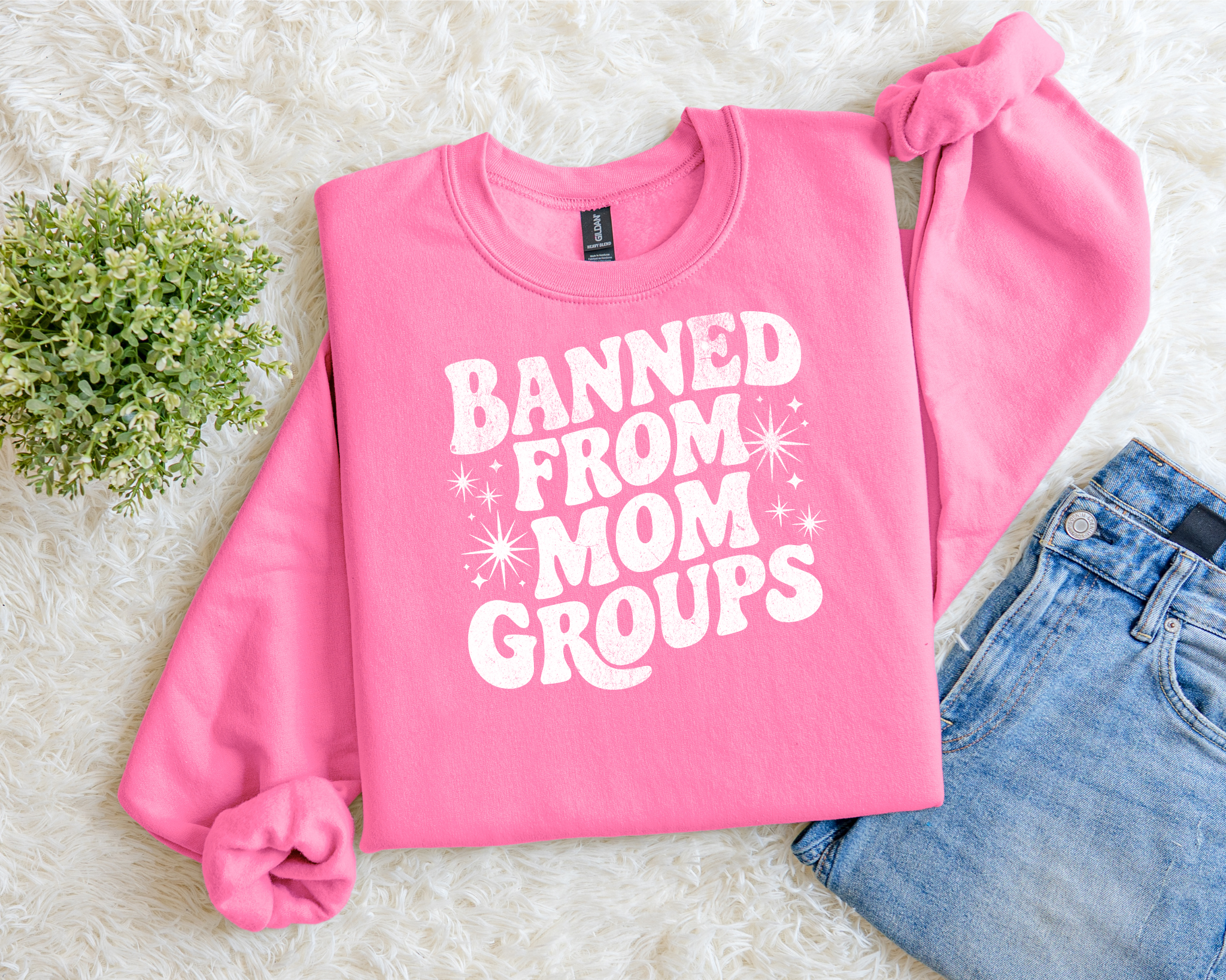 Light pink sweatshirt with bold white text reading “Banned From Mom Groups” in a retro, playful font with star accents.
