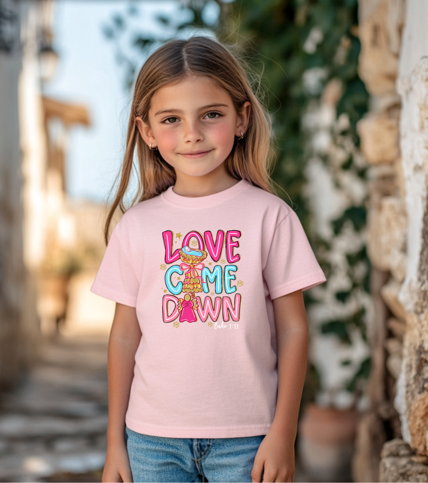 Light pink youth t-shirt with colorful “Love Came Down” design and Luke 2:11 verse, styled flat with jeans, shoes, and a holiday-inspired look.