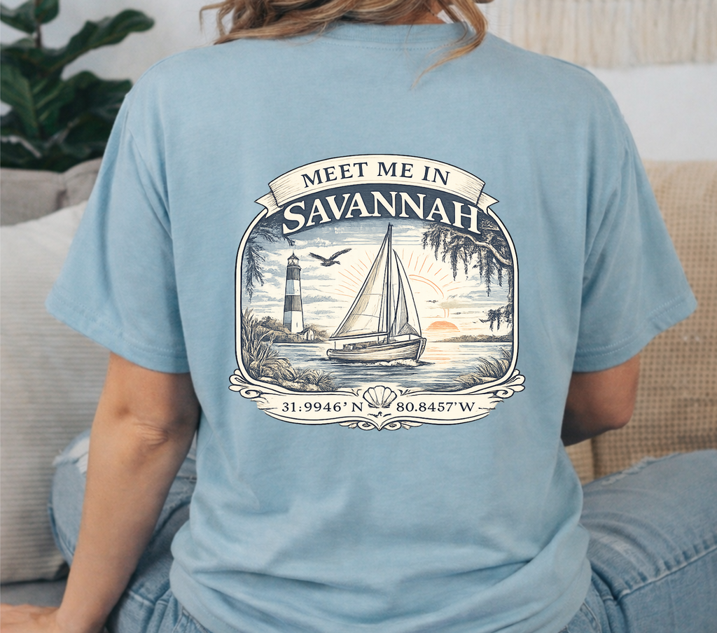 Light blue t-shirt with 'Meet Me in Savannah' graphic on the back, worn by a person sitting on a couch.