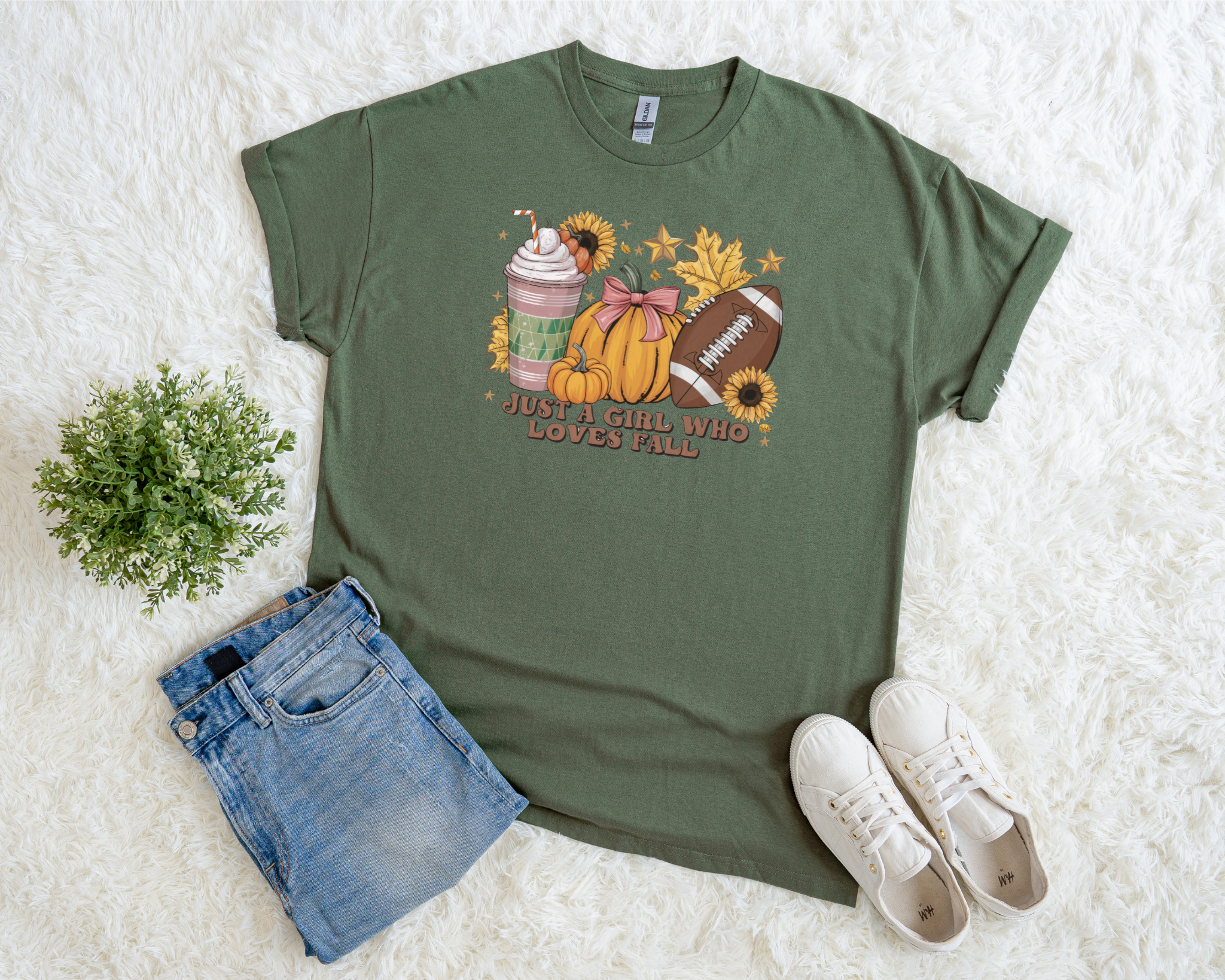 Green t-shirt with autumn-themed design, denim shorts, and white sneakers on a light background