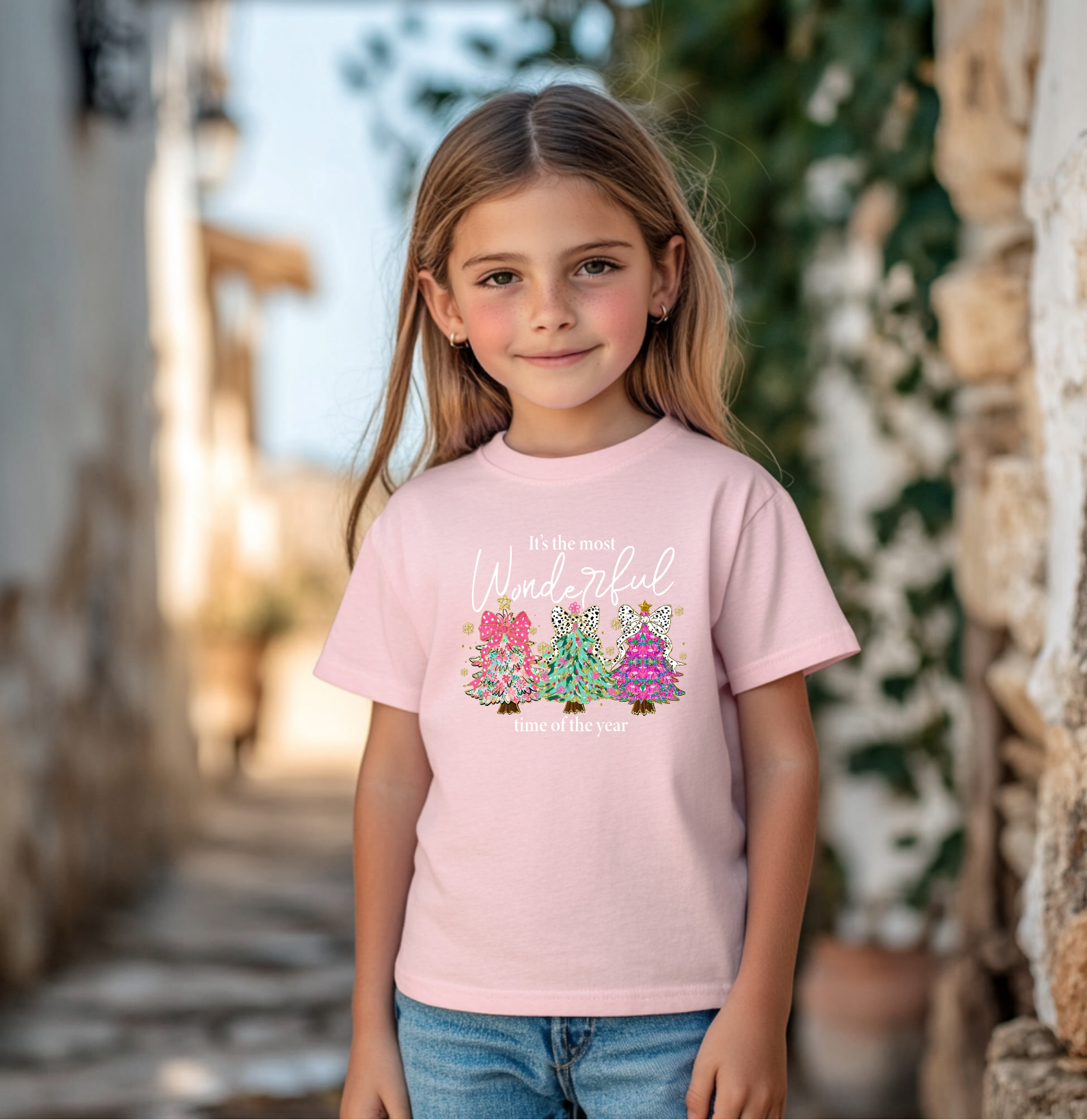 Christmas t-shirt with colorful trees and leopard bows that reads “It’s the Most Wonderful Time of the Year,” sitting happily near a decorated Christmas tree with presents.
