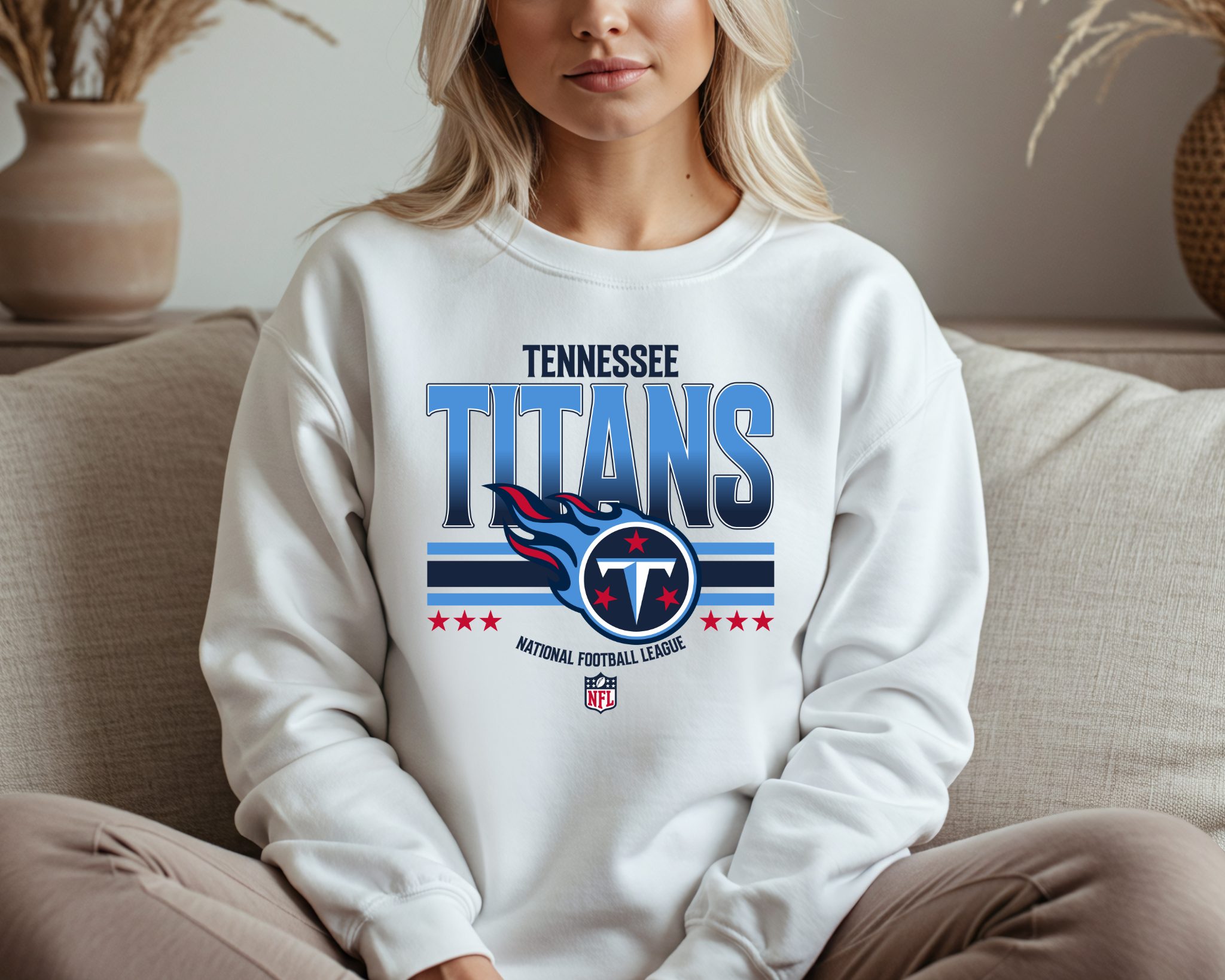 A woman wearing a white Tennessee Titans-inspired crewneck sweatshirt with bold blue and red team-style graphics, sitting comfortably on a couch.