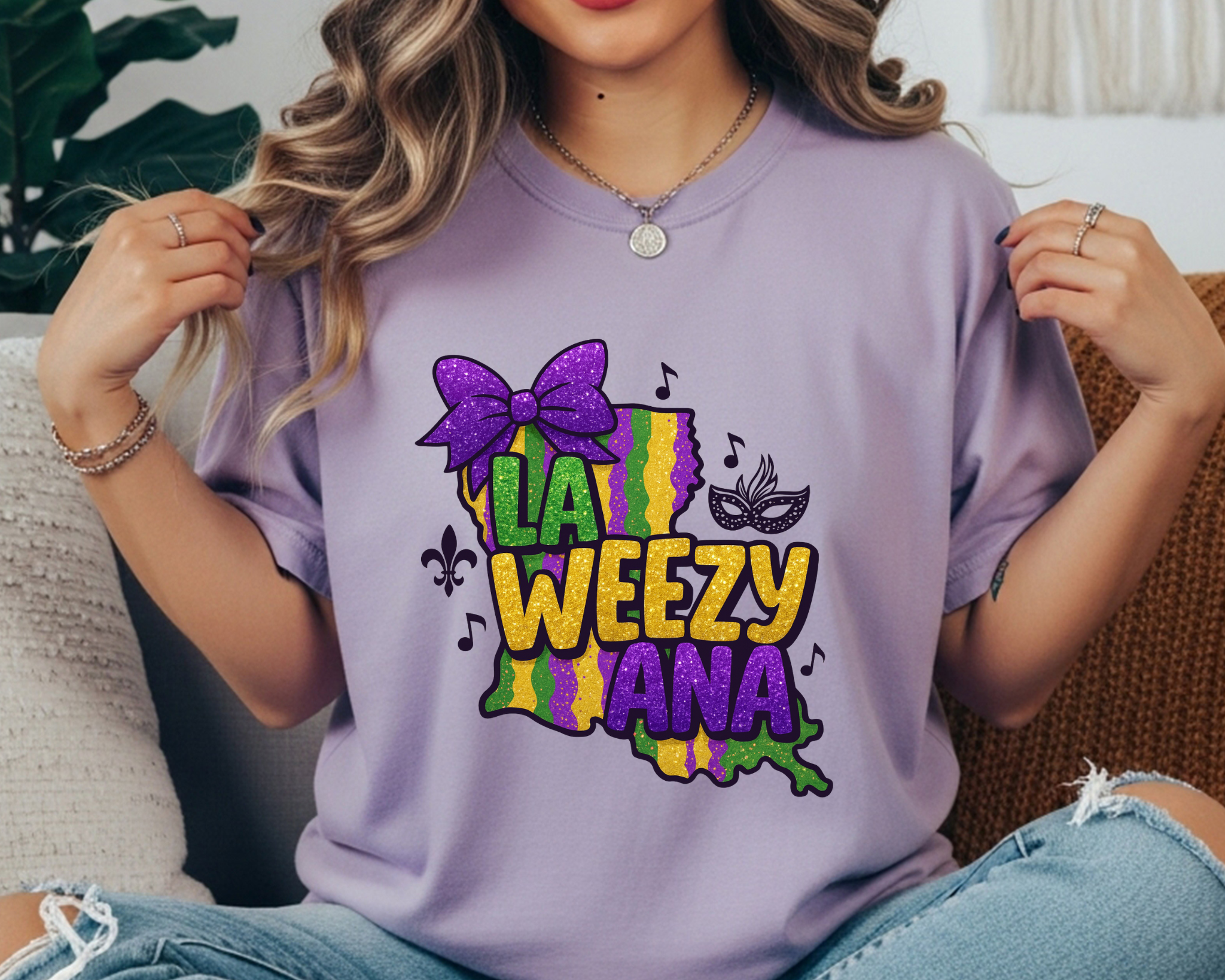 La Weezy Ana Mardi Gras t-shirt with a glitter-style Louisiana state graphic, purple bow, mask, music notes, and fleur-de-lis in purple, green, and gold