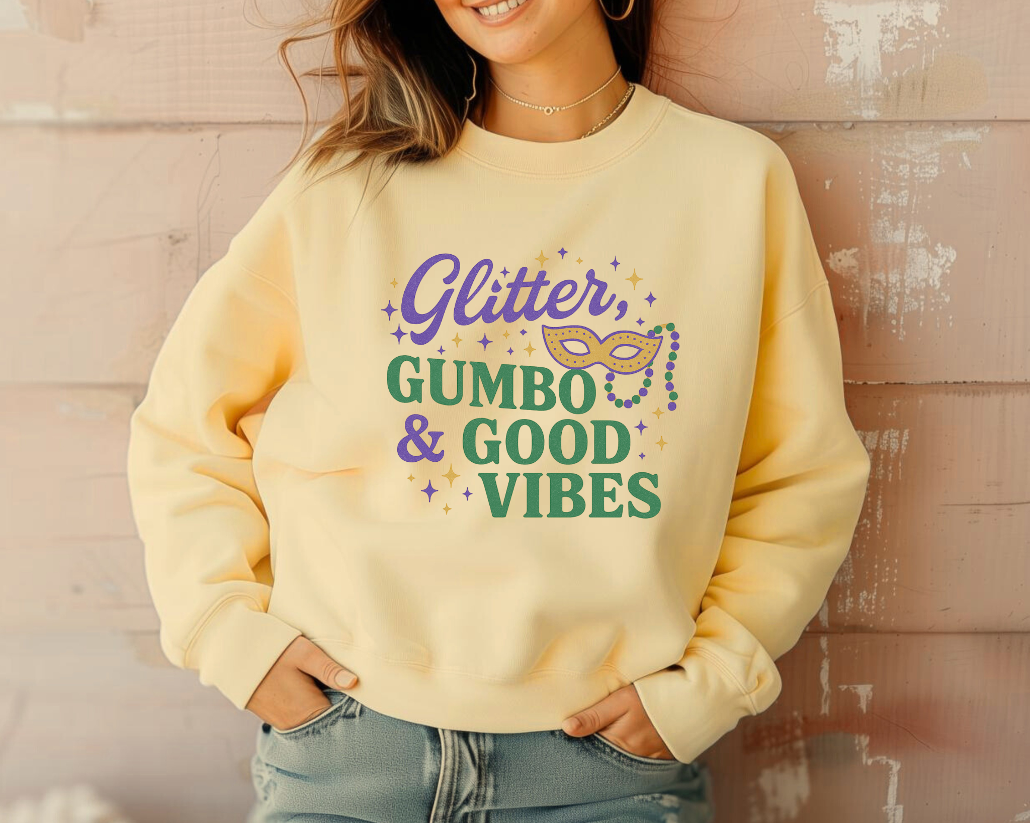 Woman wearing a yellow Comfort Colors crewneck sweatshirt featuring a Mardi Gras “Glitter, Gumbo & Good Vibes” graphic in purple, green, and gold.