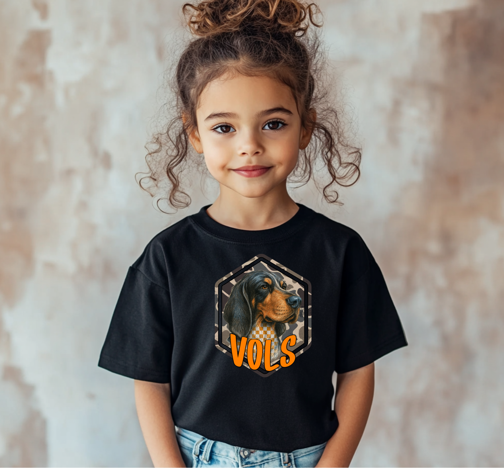 Youth camo Smokey VOLS t-shirt featuring a hound dog graphic with a checkerboard and camo background, and bold orange “VOLS” lettering. Perfect soft tee for kids’ game-day style or school spirit wear.