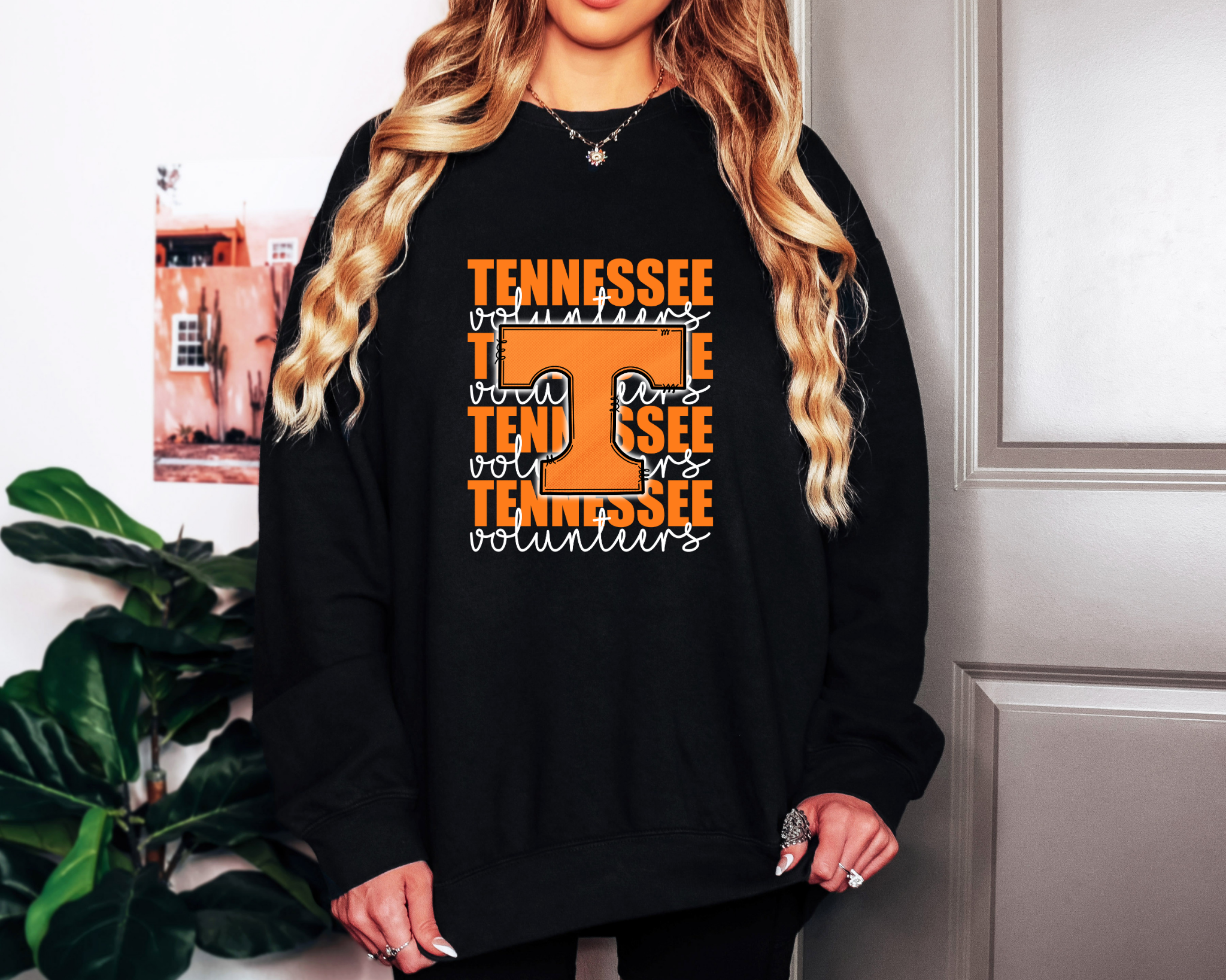 Model wearing a black Comfort Colors sweatshirt featuring a bright orange “T” and repeating “Tennessee Volunteers” text in white script — retro boutique game day style.