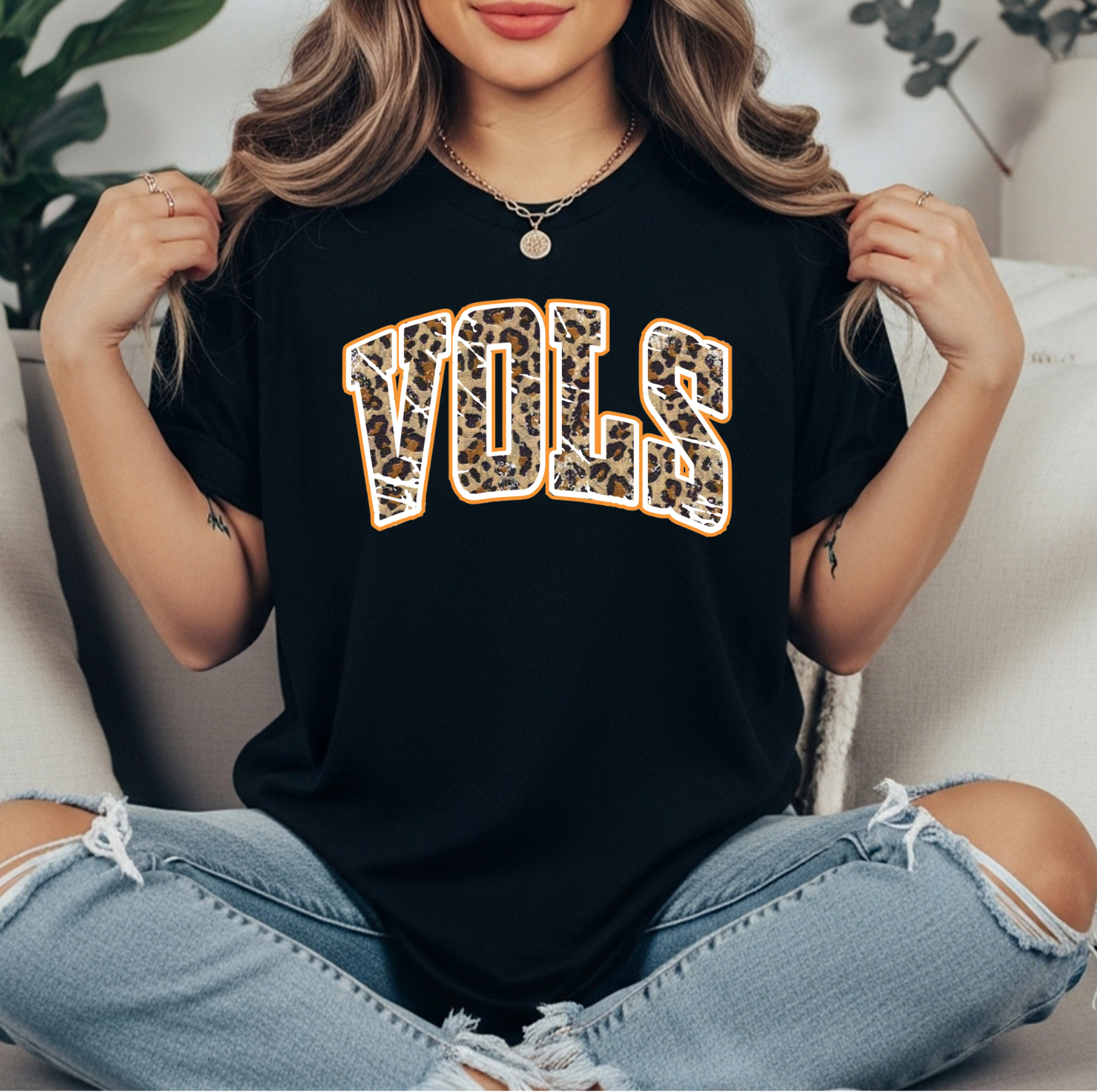 Leopard print VOLS graphic t-shirt on a black comfort Colors tee, displayed flat lay style with jeans, sneakers, and a small green plant on a white fluffy rug. Perfect casual game day look for Tennessee fans.