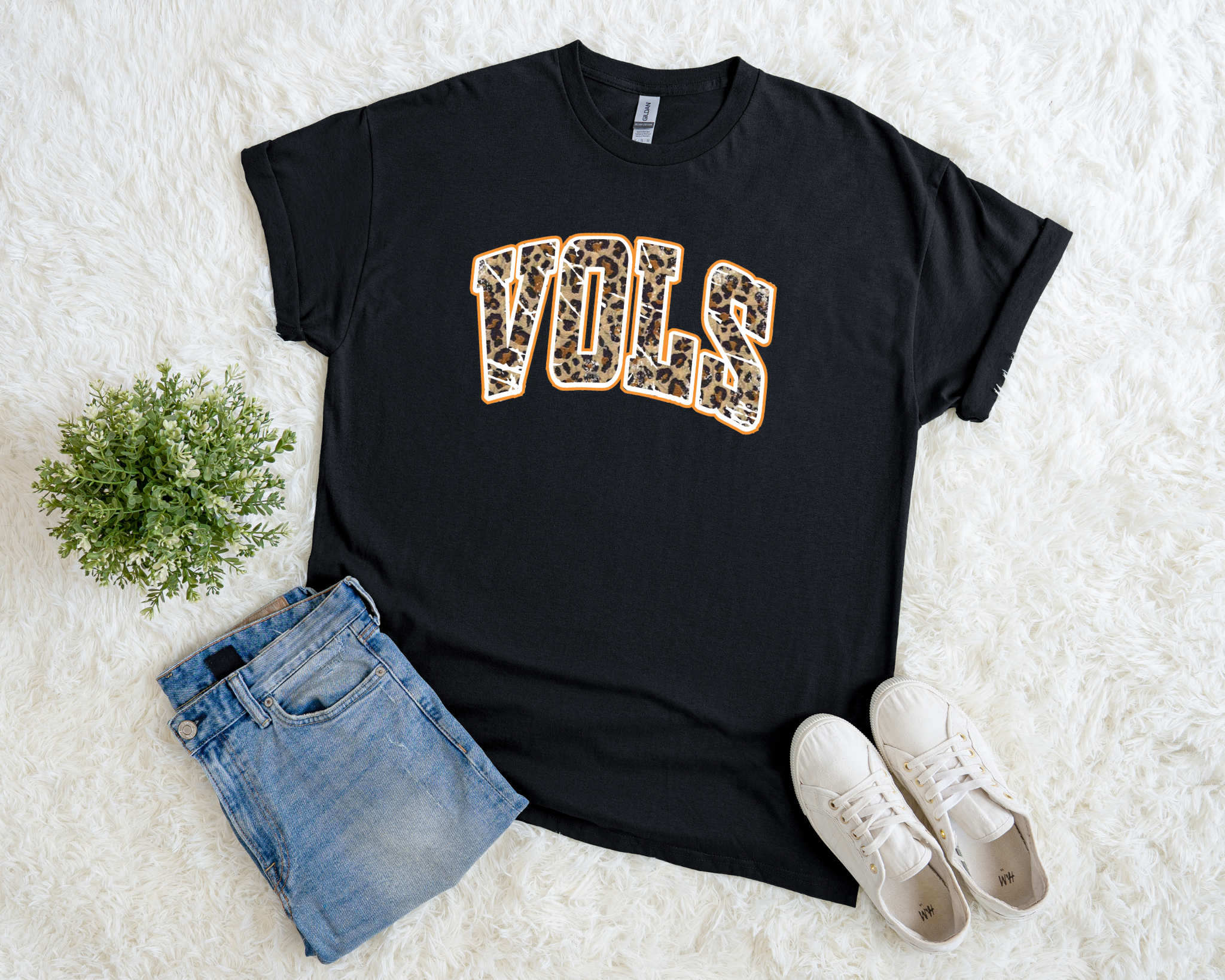black t-shirt with leopard print “VOLS” design outlined in orange, styled flat with denim jeans and white sneakers.