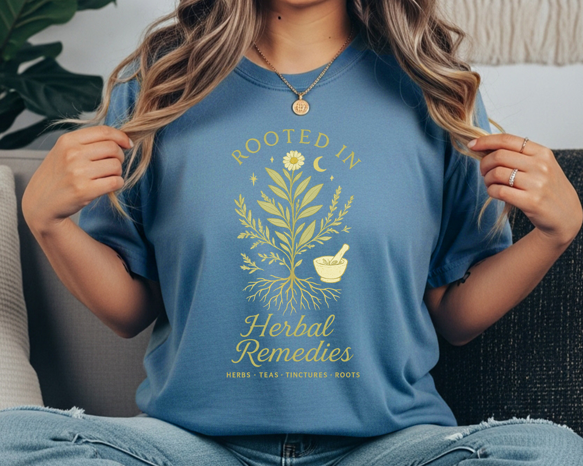 blue jean Comfort Colors t-shirt with a yellow botanical design of herbs and roots, a mortar and pestle, crescent moon, and the text “Rooted in Herbal Remedies – Herbs • Teas • Tinctures • Roots.”