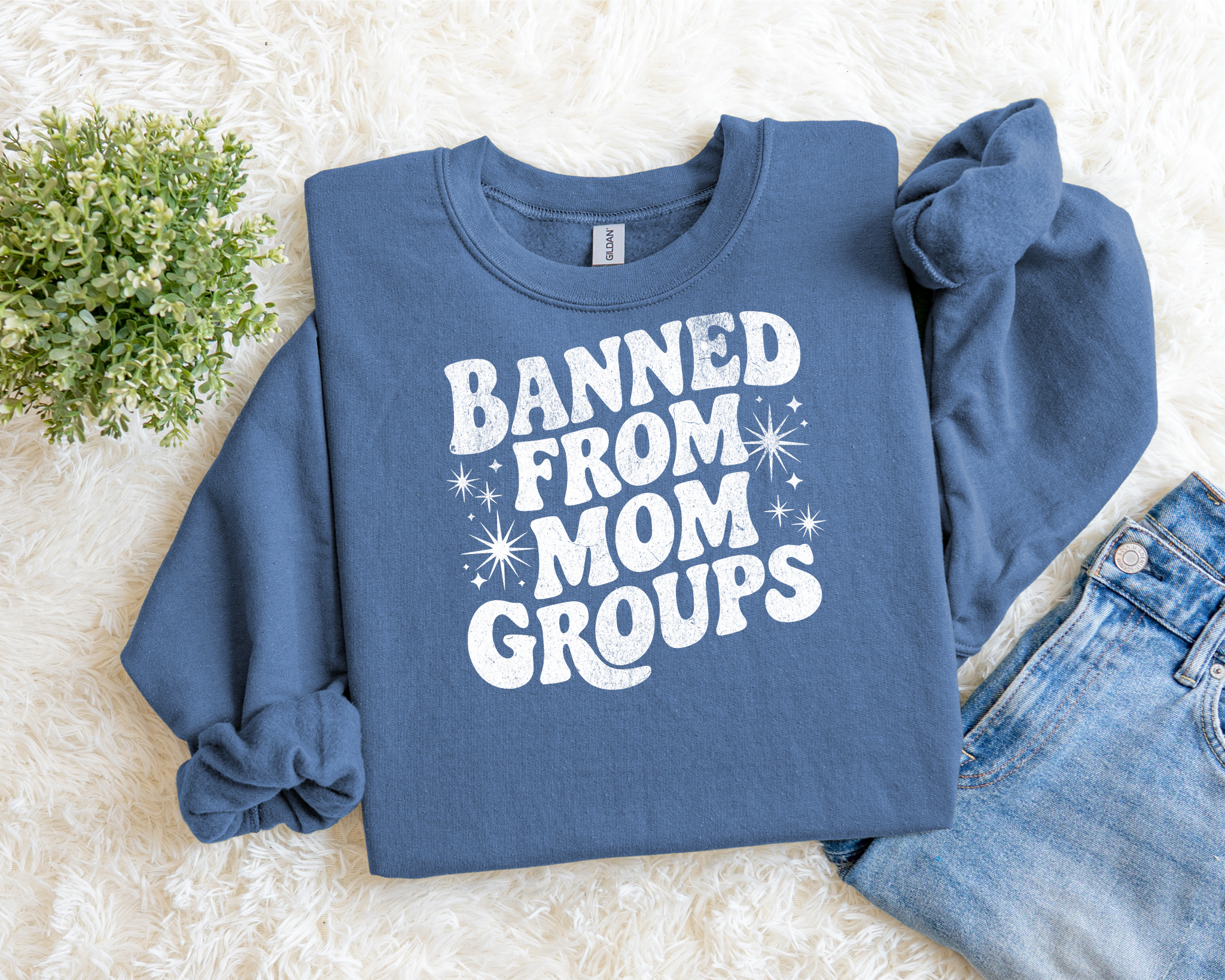 blue sweatshirt with bold white text reading “Banned From Mom Groups” in a retro, playful font with star accents.