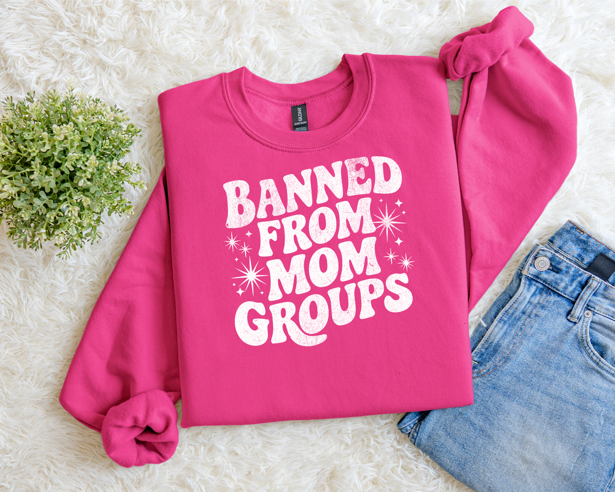 bright pink sweatshirt with bold white text reading “Banned From Mom Groups” in a retro, playful font with star accents.
