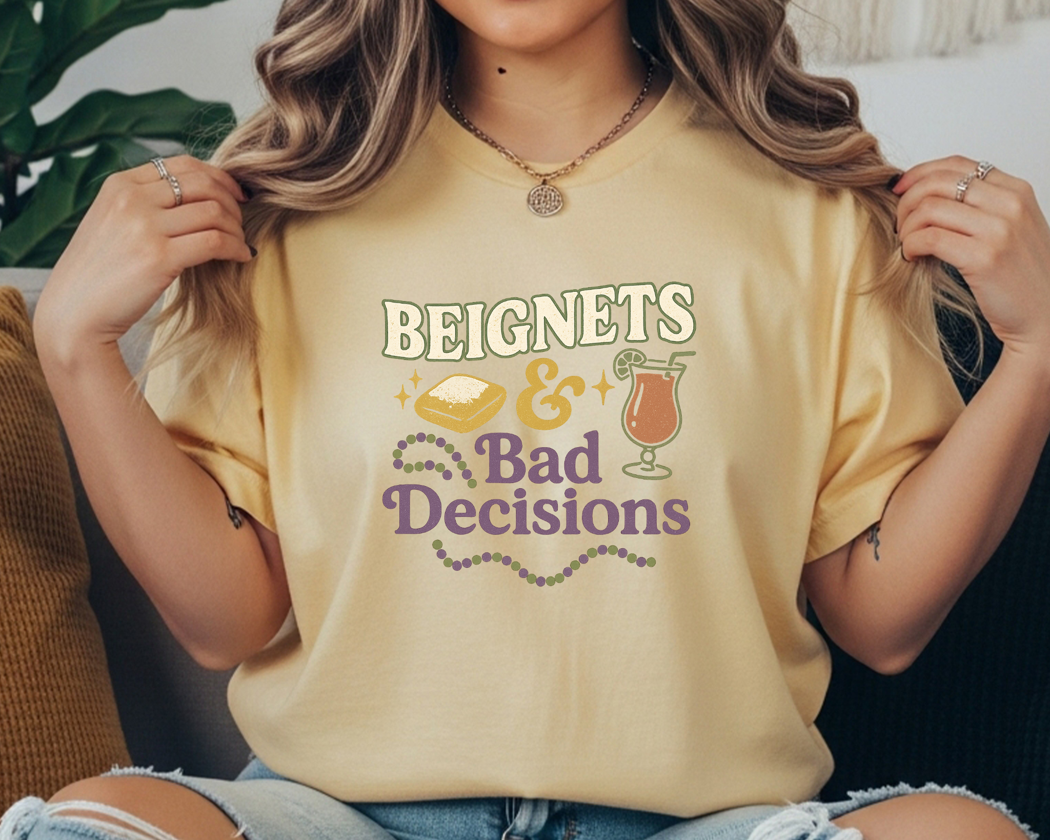 butter Comfort Colors tee with Mardi Gras design featuring beignet, cocktail, and text reading “Beignets & Bad Decisions” in purple, gold, and green.