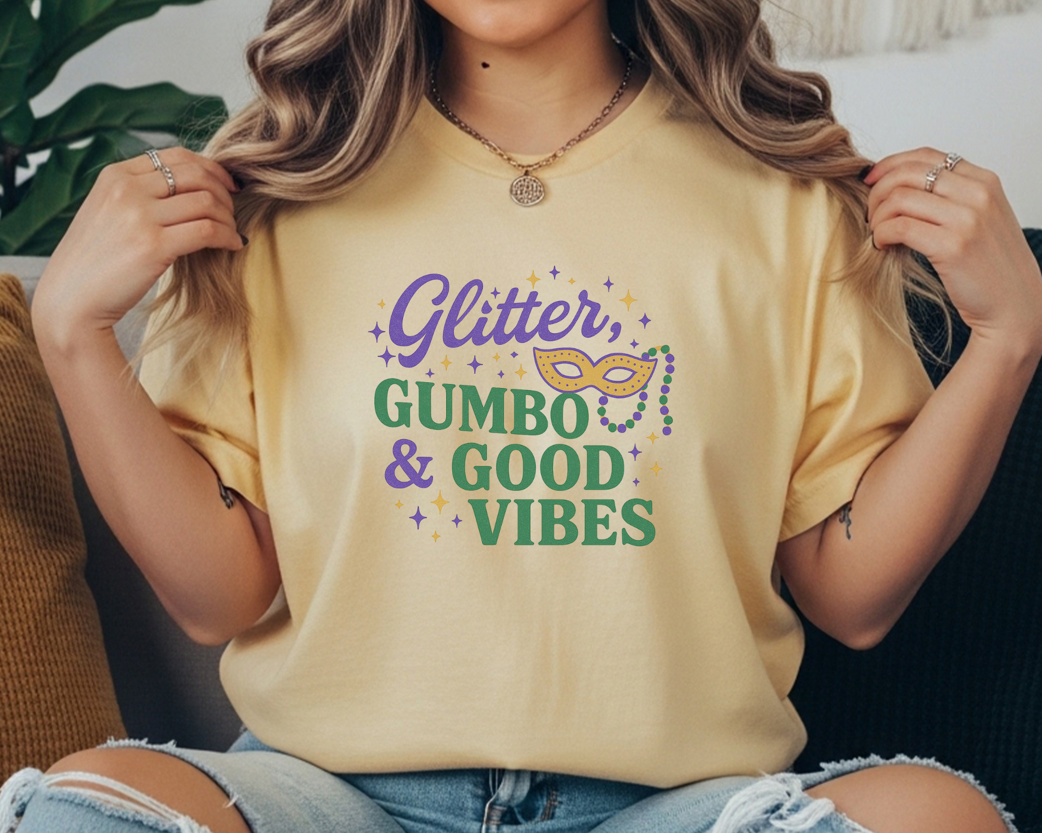 butter Comfort Colors tee with green and gold text reading “Glitter, Gumbo & Good Vibes” and a Mardi Gras mask with beaded accents.