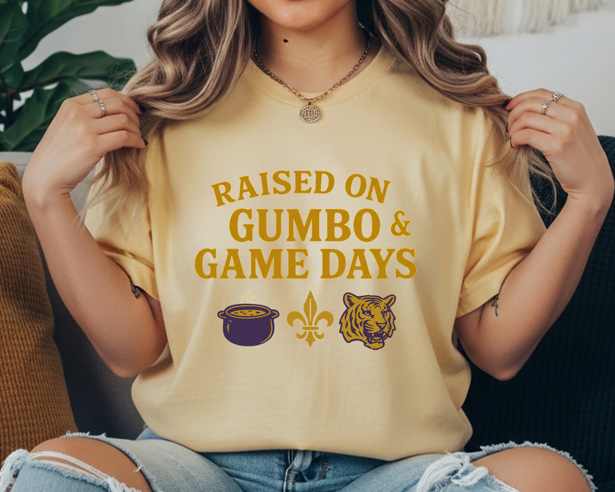 butter Comfort Colors tee with “Raised on Gumbo & Game Days” text and icons of a gumbo pot, fleur-de-lis, and tiger in gold and purple.