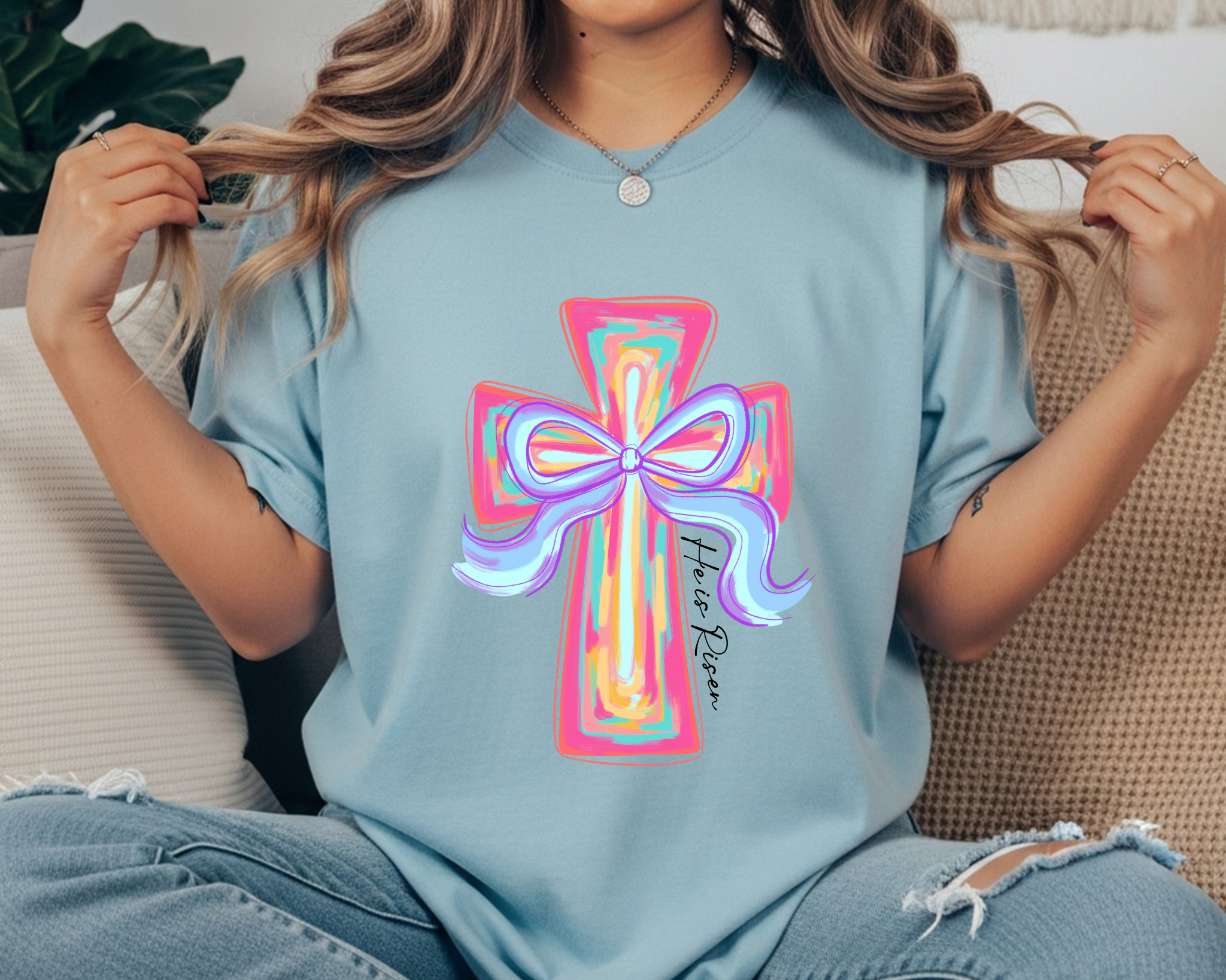 Comfort Colors t-shirt featuring a colorful pastel cross with a bow and “He Is Risen” script printed vertically along the cross.