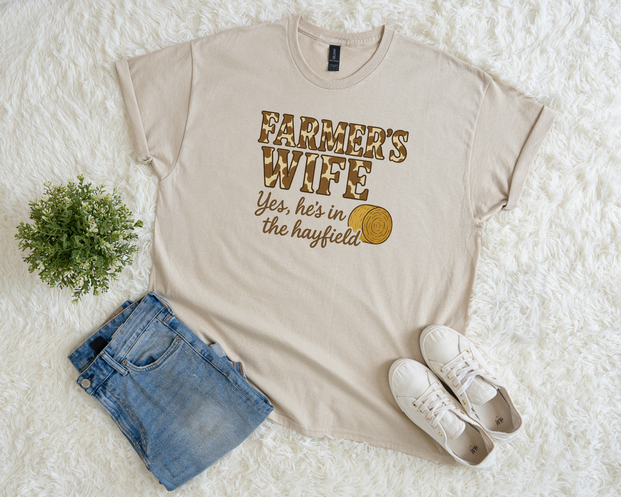 Beige t-shirt with 'Farmer's Wife' text, blue shorts, white sneakers, and a plant on a white surface