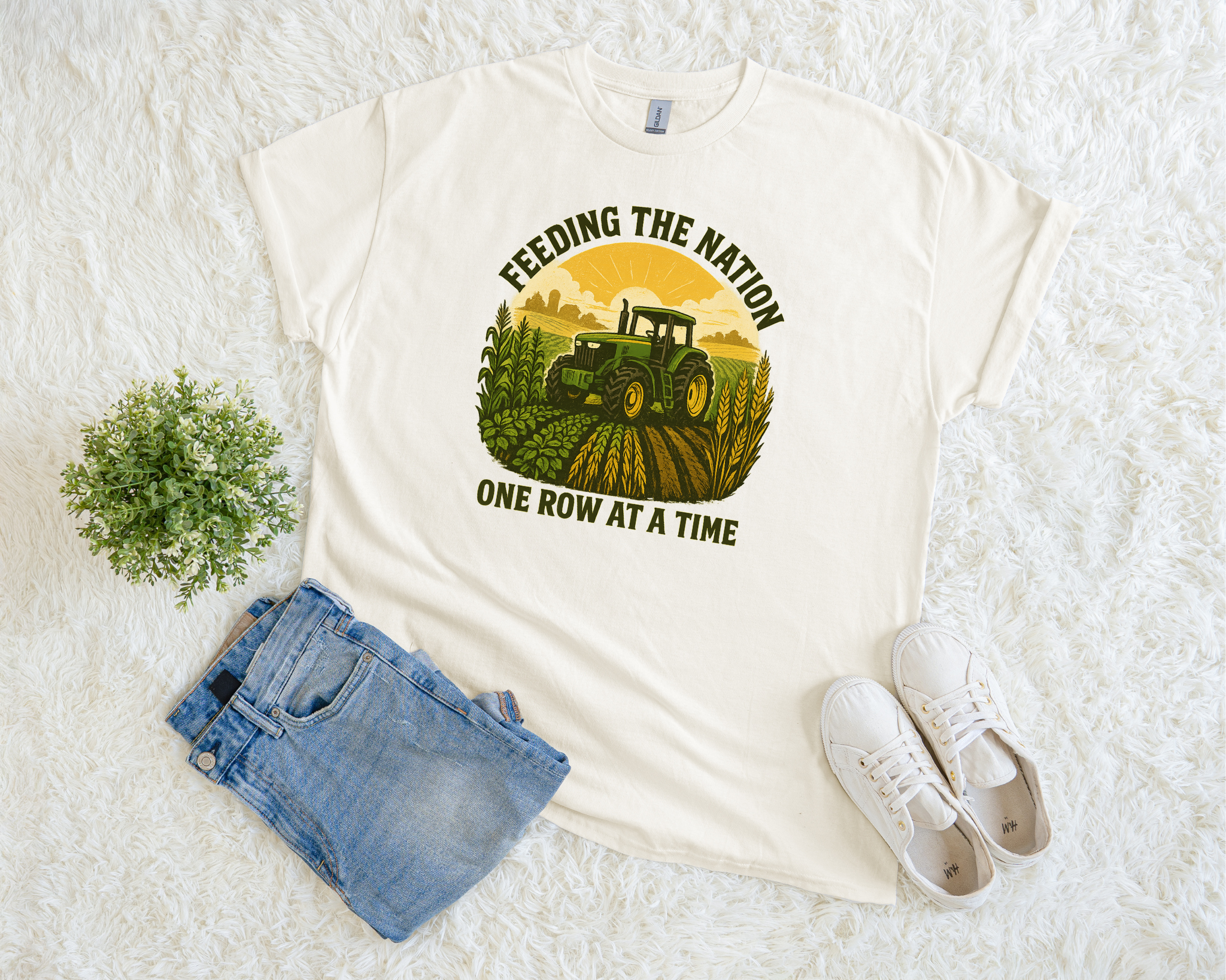 White t-shirt with a graphic of a tractor and text 'Feeding the Nation One Row at a Time' on a white surface with jeans and sneakers.
