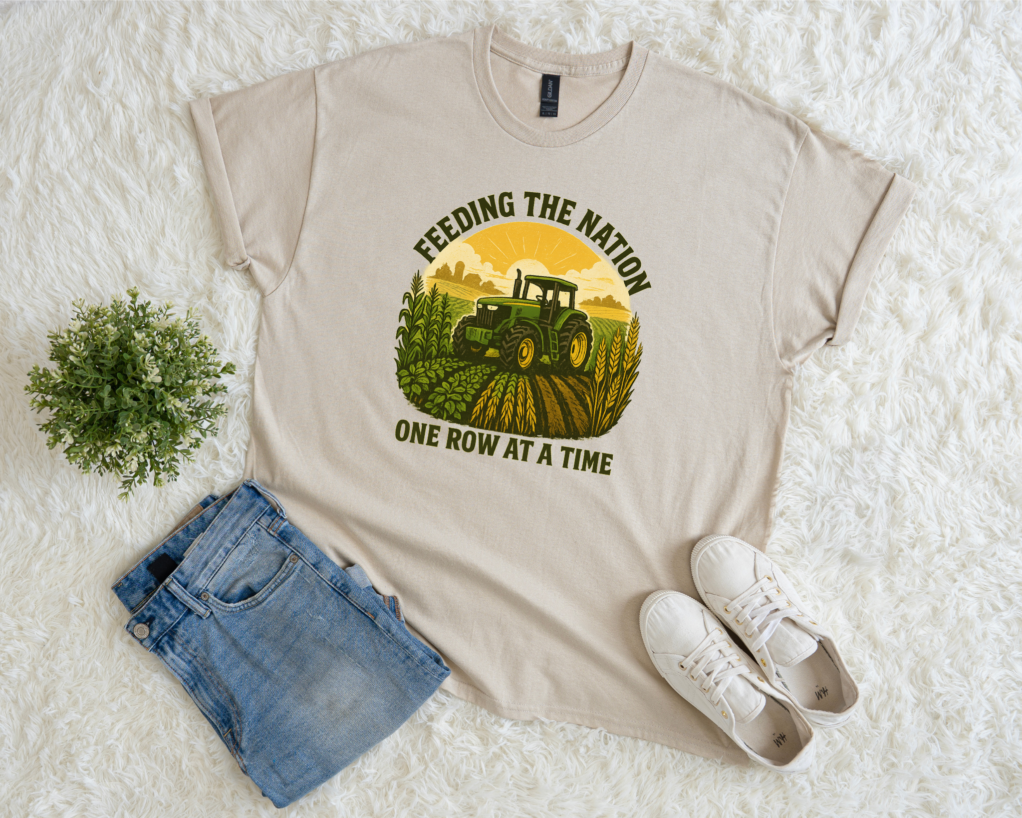 Beige t-shirt with a graphic of a tractor and text, paired with denim shorts and white sneakers on a textured white surface.