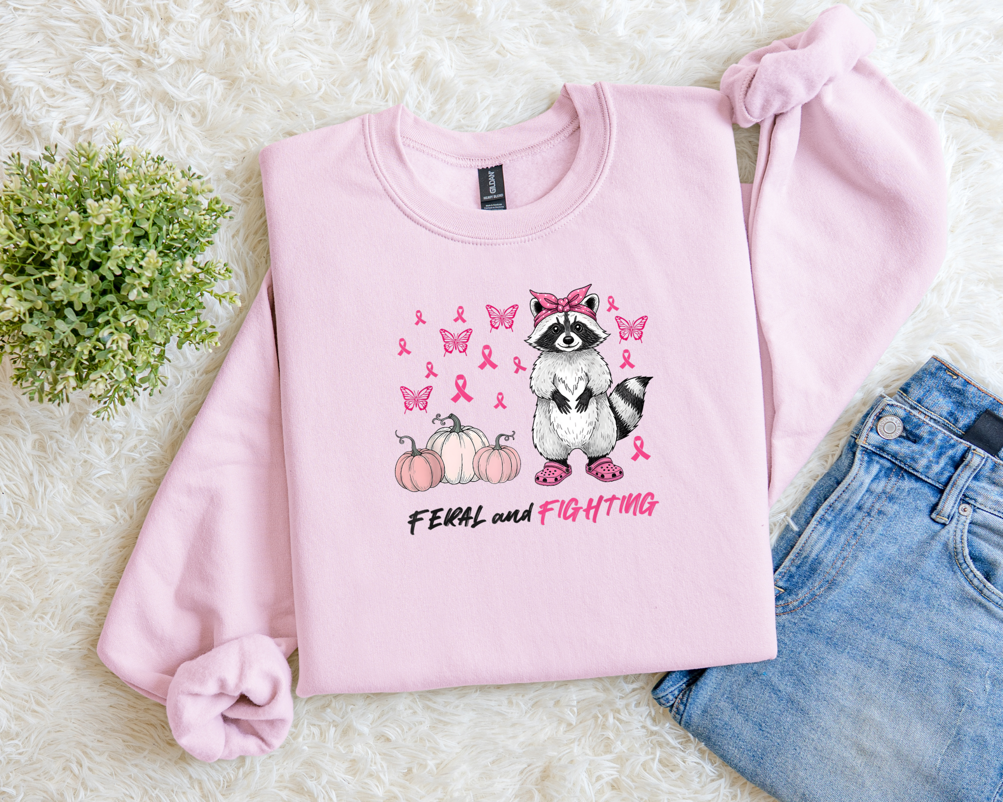 Pink sweatshirt with raccoon and cancer awareness design on a light background