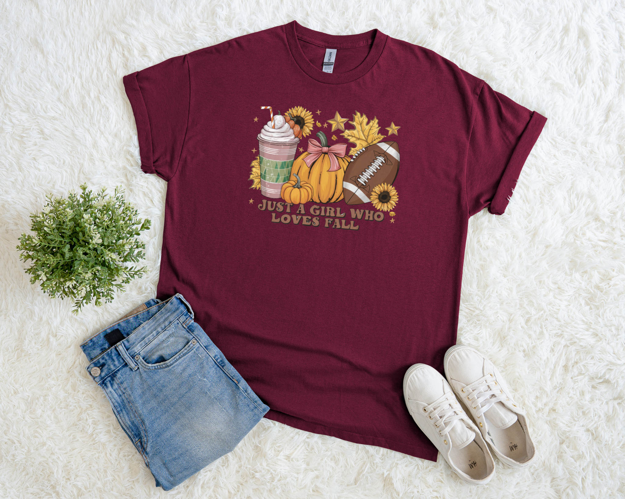 Maroon t-shirt with fall-themed design, denim shorts, and white sneakers on a white surface.