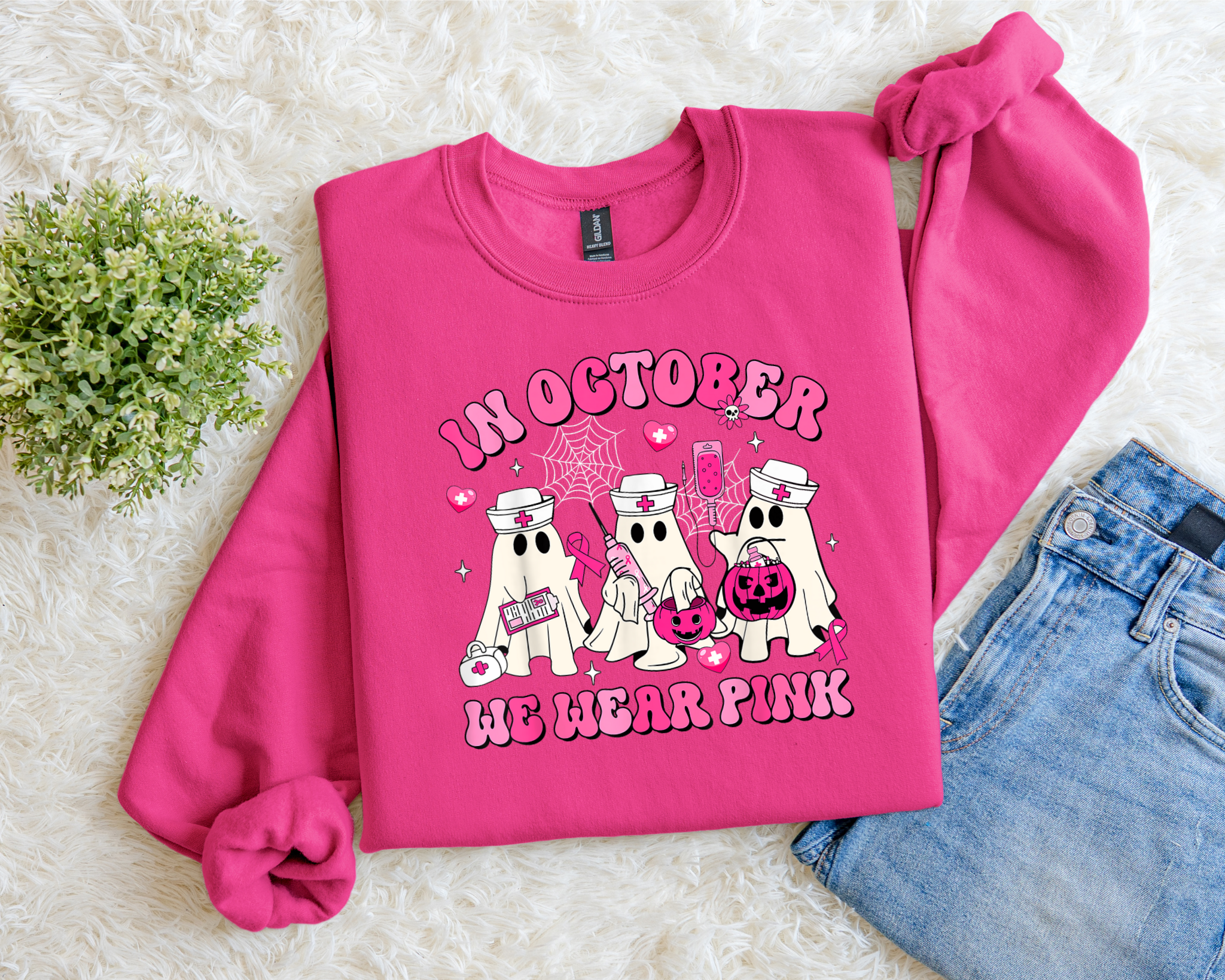 Pink sweatshirt with Halloween-themed design on a textured surface with jeans and flowers.