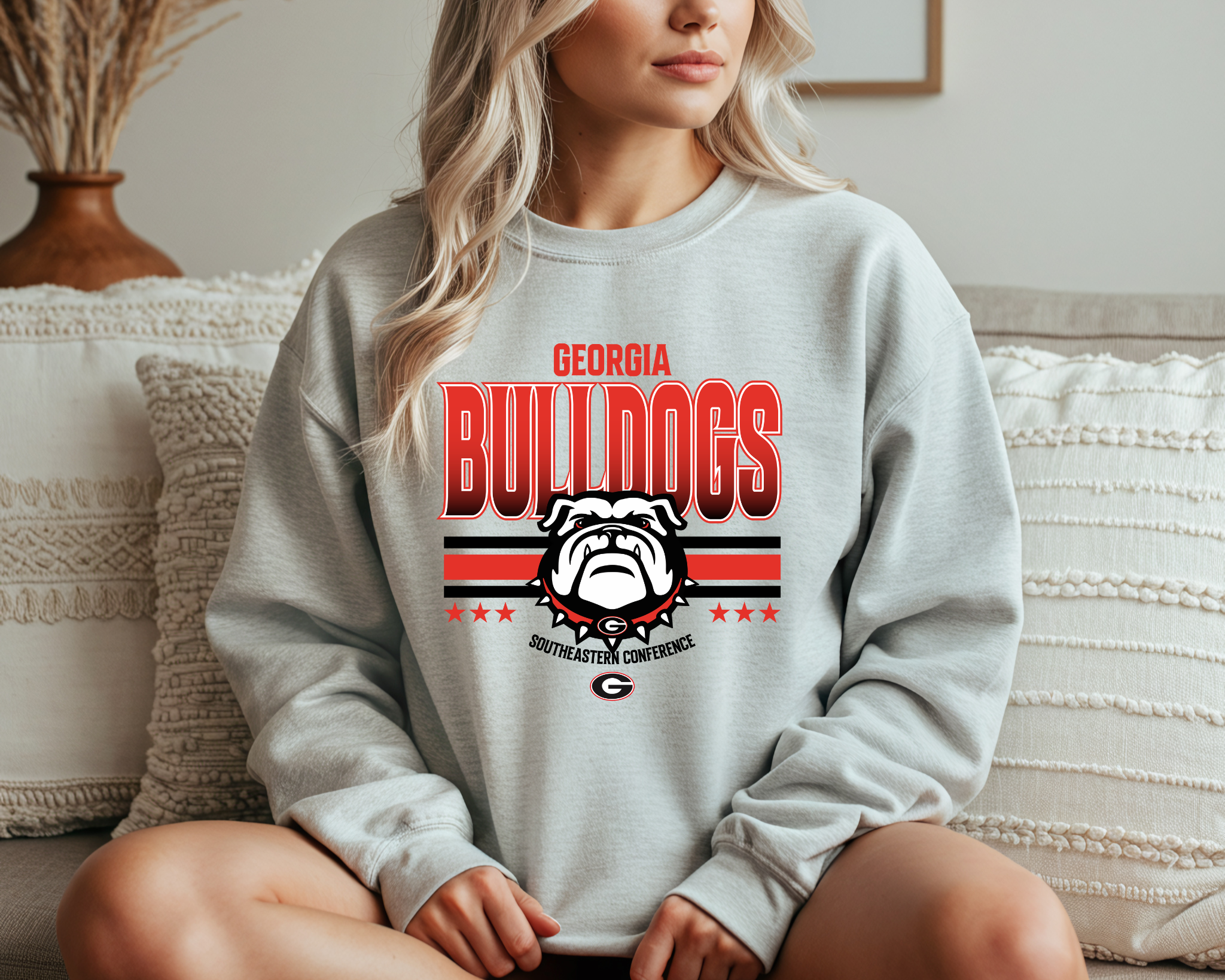 A woman wearing a Georgia Bulldogs-inspired crewneck sweatshirt featuring bold red and black graphics with a fierce bulldog design, sitting comfortably on a couch.