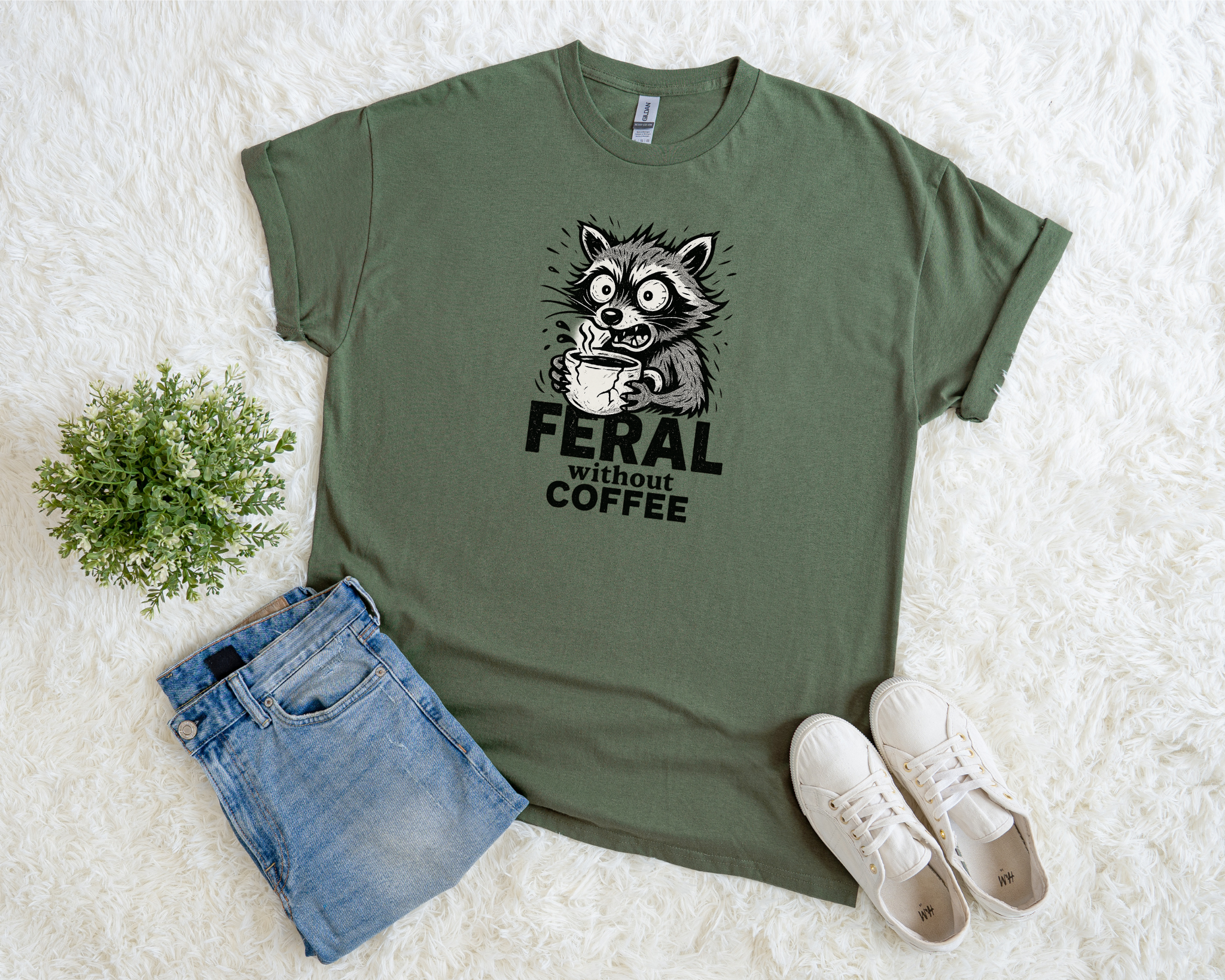 Green t-shirt with a raccoon graphic and text, paired with denim shorts and white sneakers on a light background.