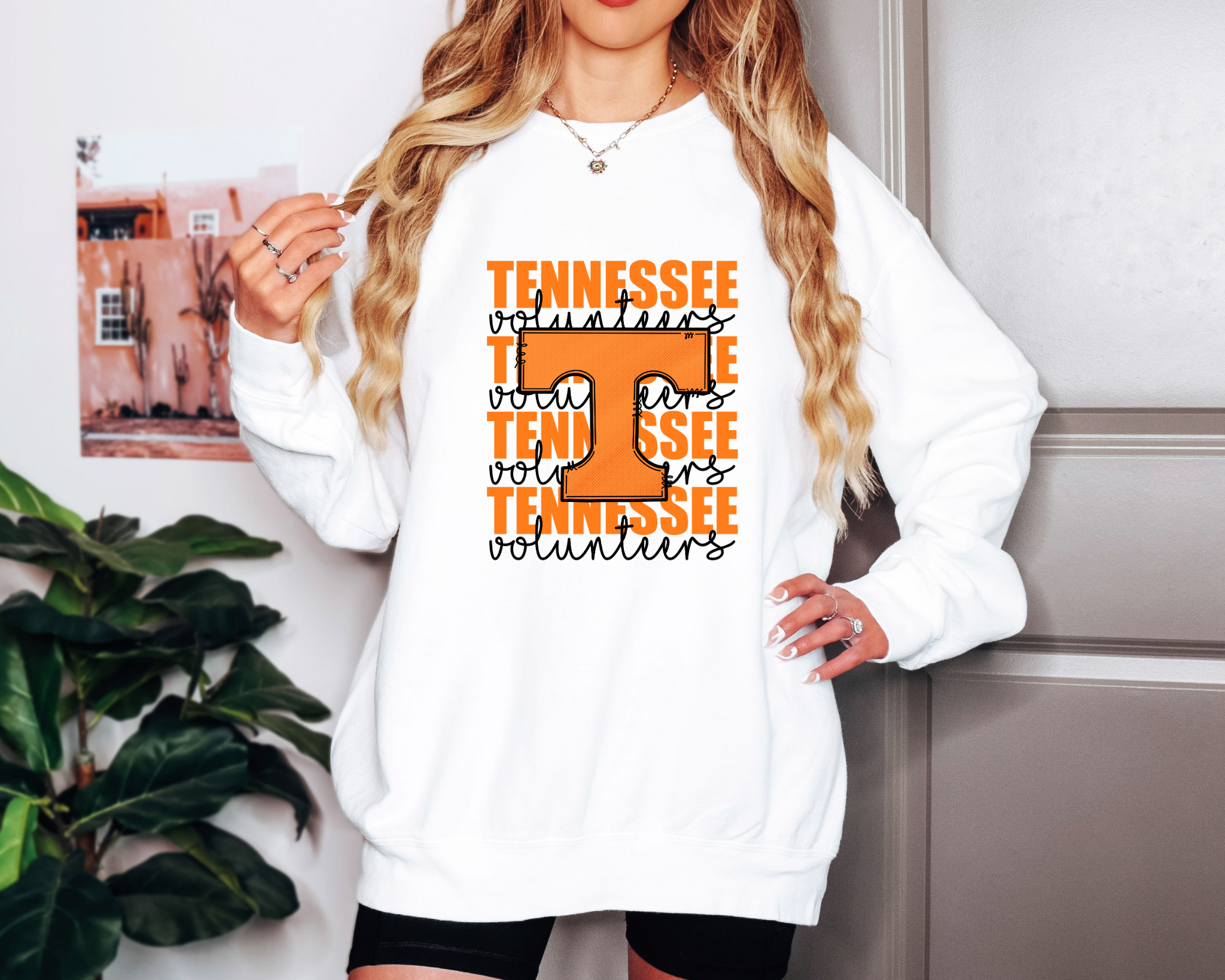 Model wearing a white Comfort Colors sweatshirt with bold orange “T” layered over repeating “Tennessee Volunteers” text in black script — vintage-inspired game day design.