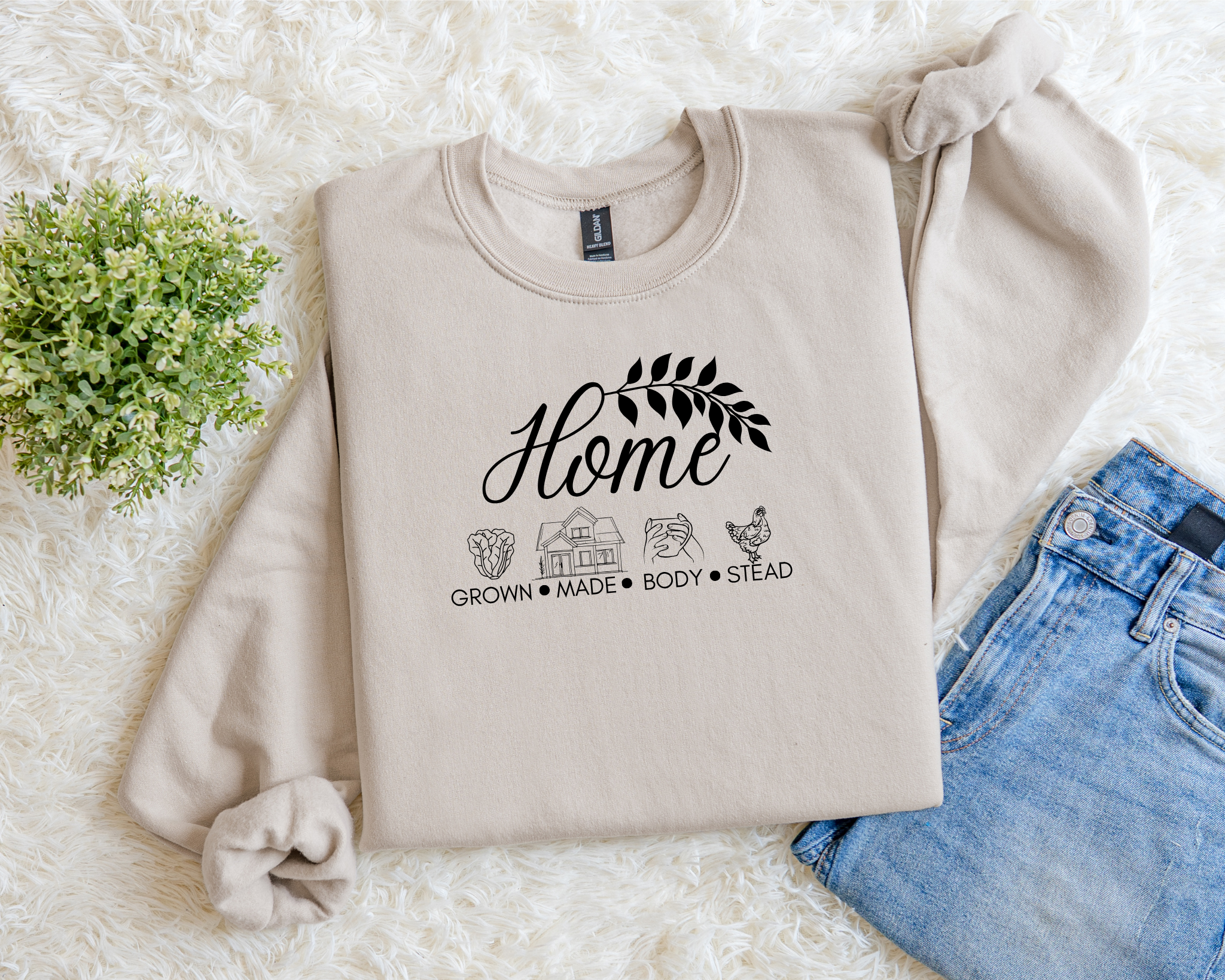 Beige sweatshirt with text and graphics on a white surface with flowers and jeans.