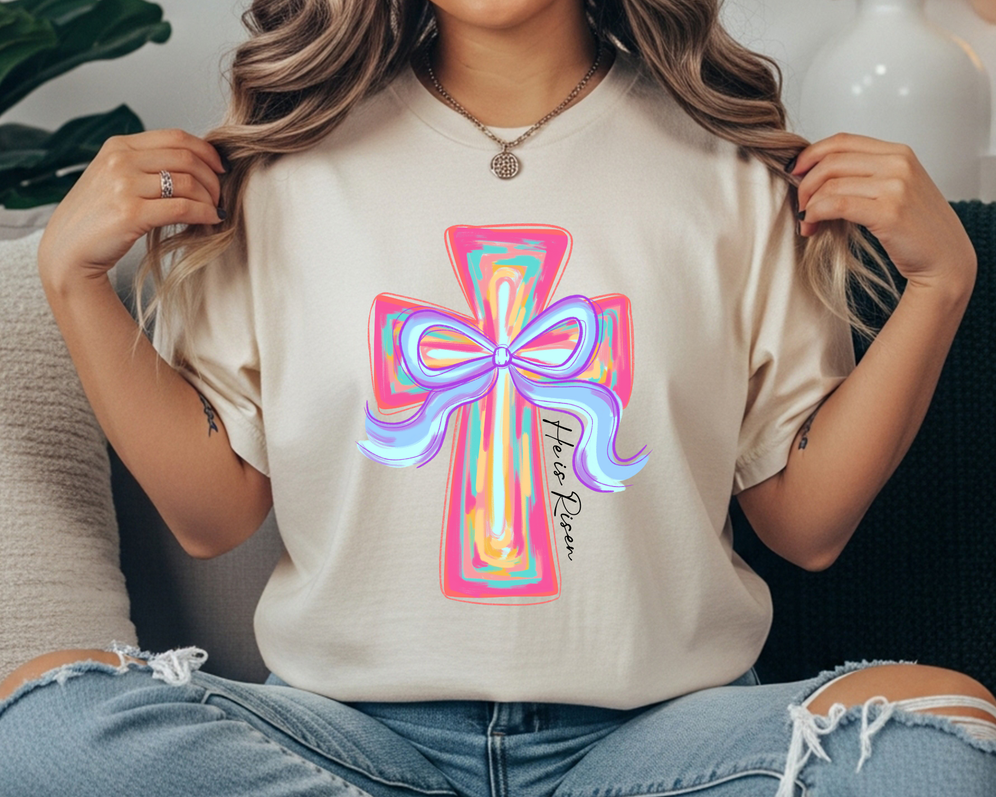 Comfort Colors t-shirt featuring a colorful pastel cross with a bow and “He Is Risen” script printed vertically along the cross.