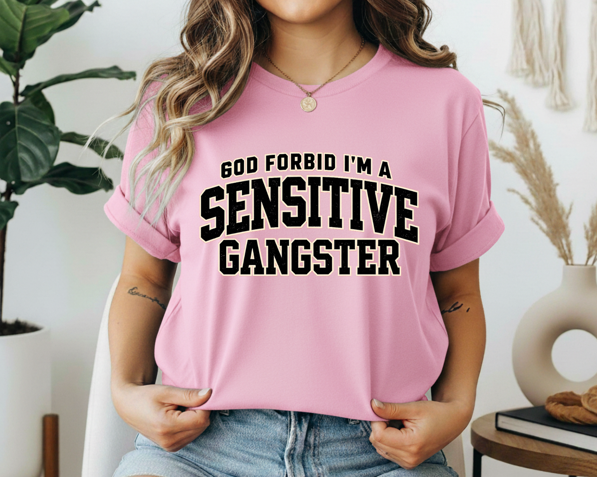 Person wearing a pink t-shirt with 'GOD FORBID I'M A SENSITIVE GANGSTER' text in a casual setting.