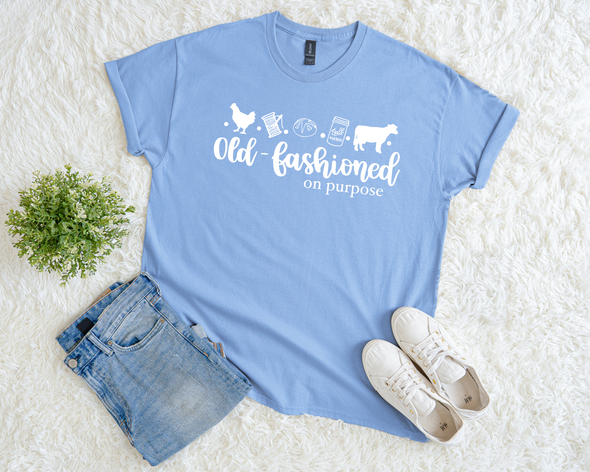 Light blue t-shirt with graphic design and text, paired with denim shorts and white sneakers on a light background.