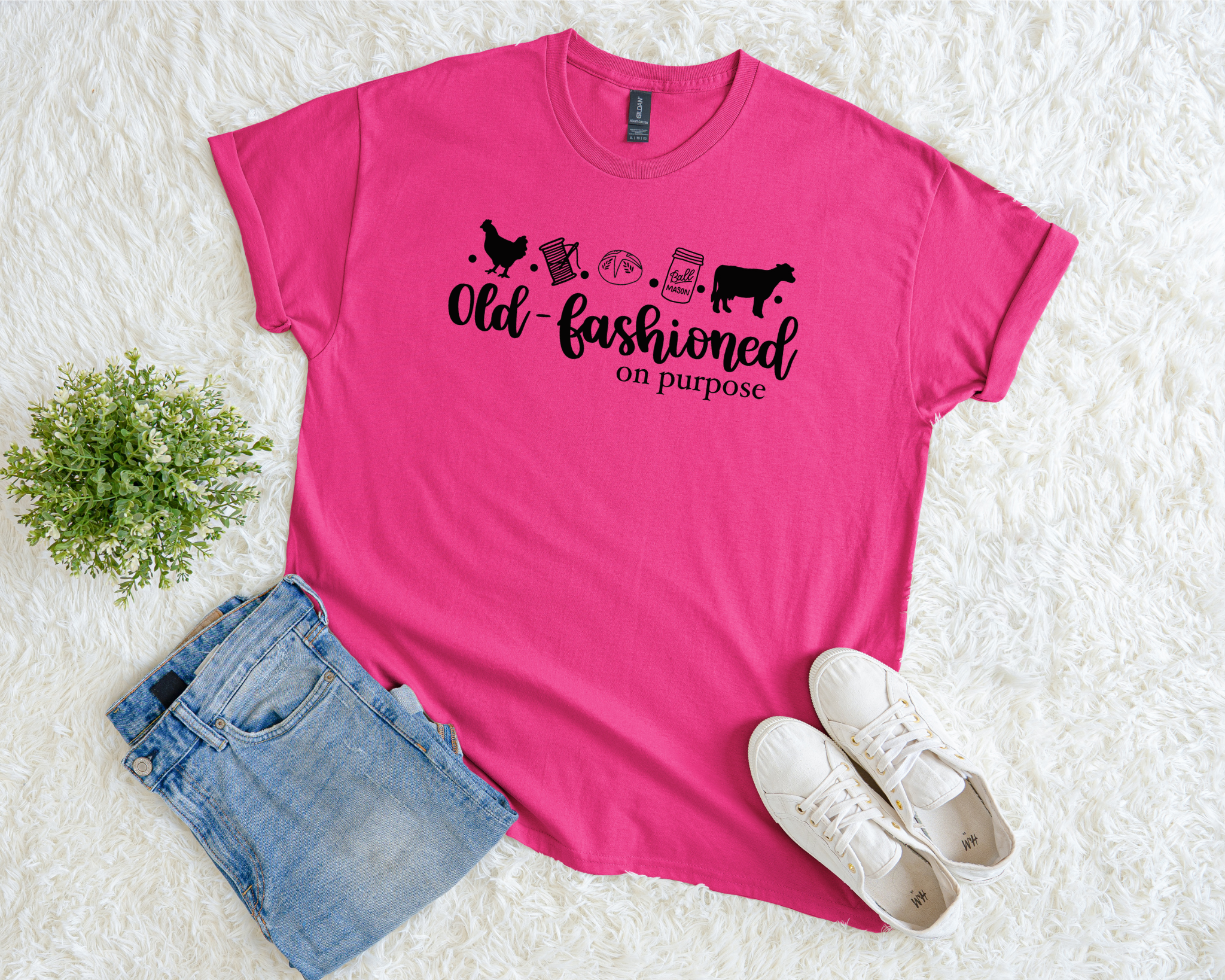 Pink t-shirt with text and graphics, paired with denim shorts and white sneakers on a textured surface.