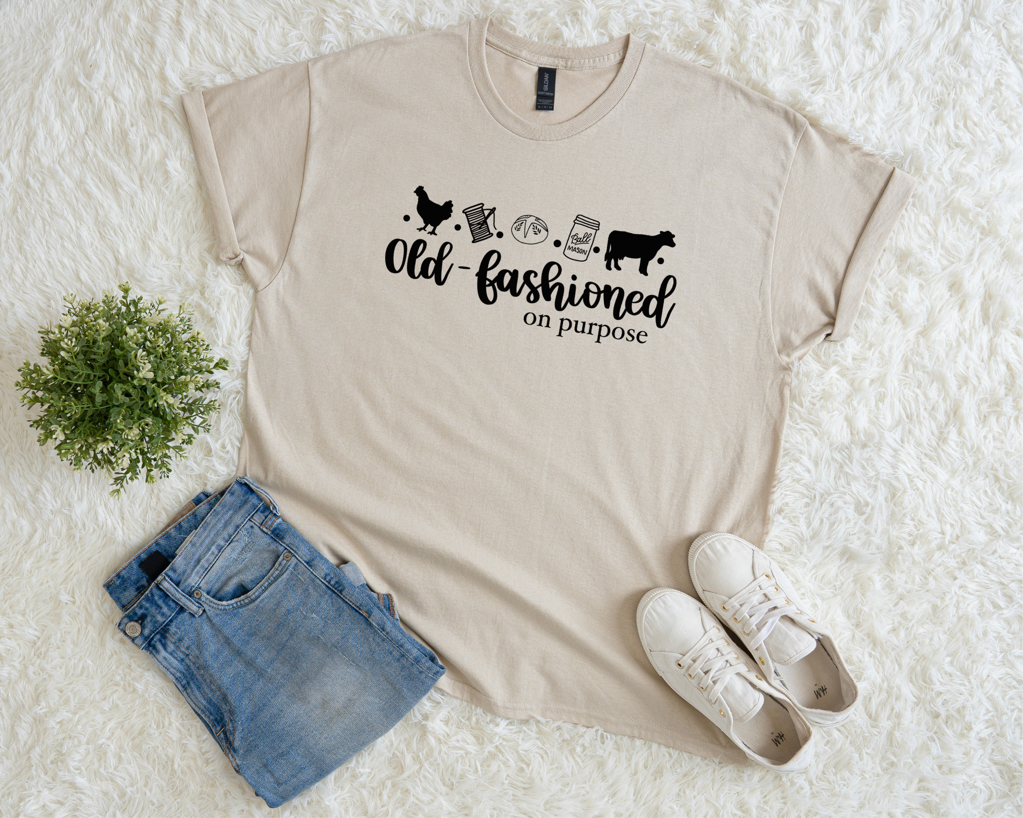 Beige t-shirt with graphic design and text, paired with denim shorts and white sneakers on a textured surface.