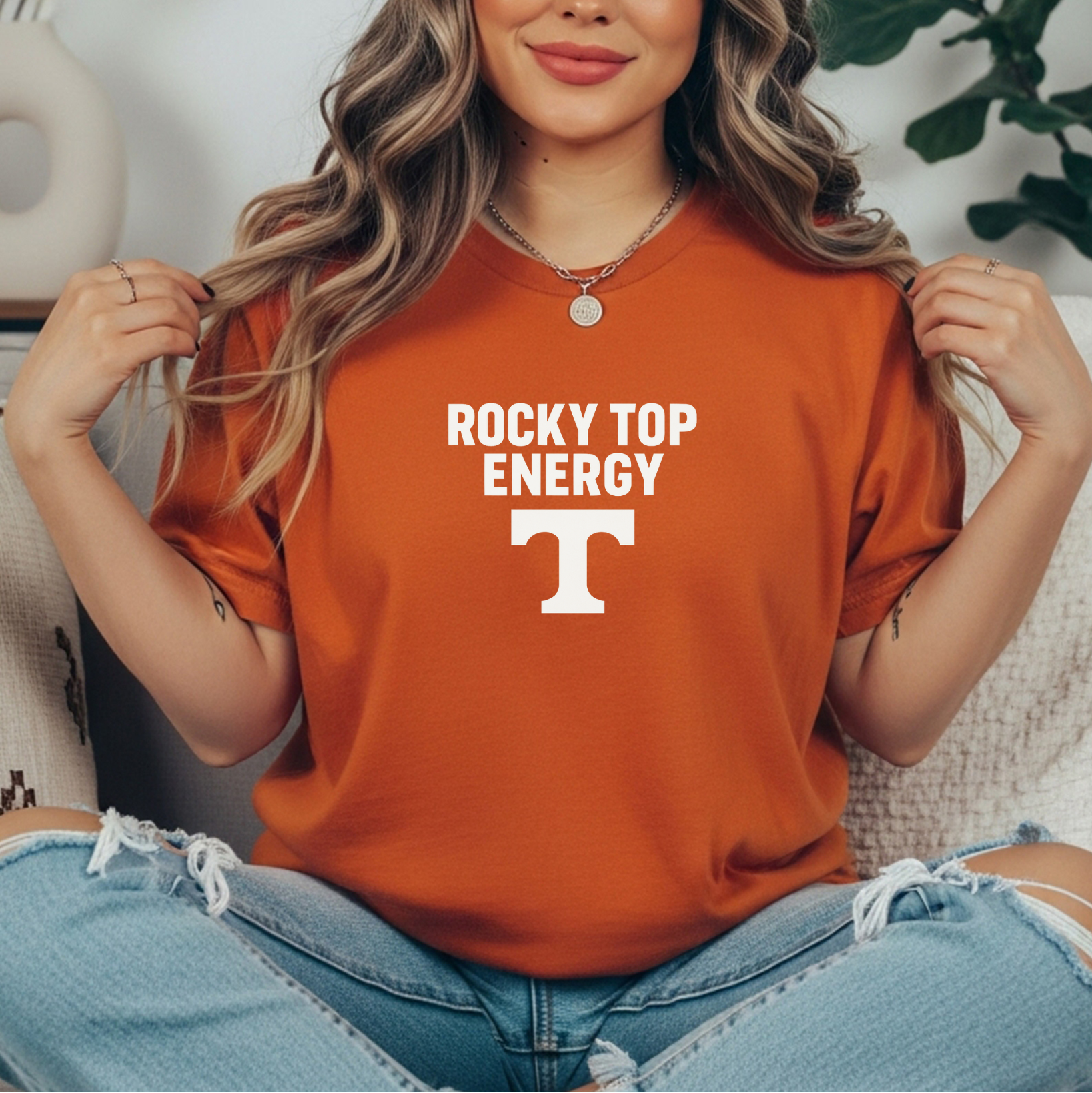 Person wearing an orange t-shirt with 'Rocky Top Energy' and a logo, sitting on a couch.