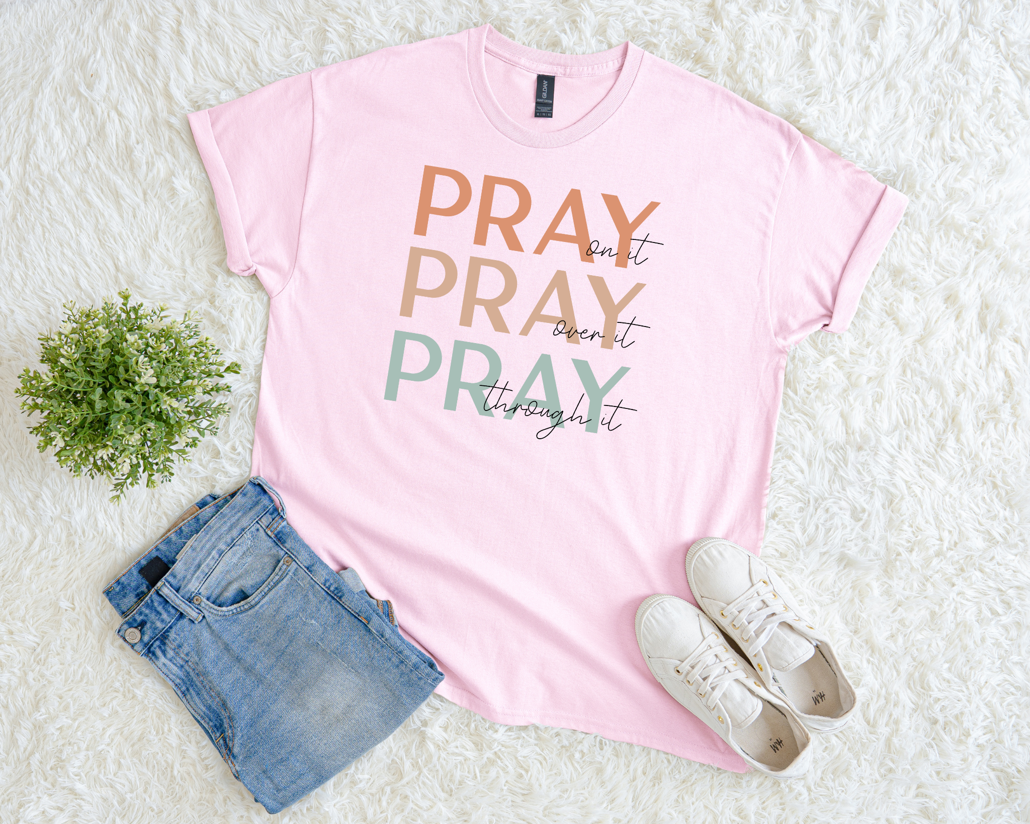 Pink t-shirt with 'PRAY' text, denim shorts, and white sneakers on a light background