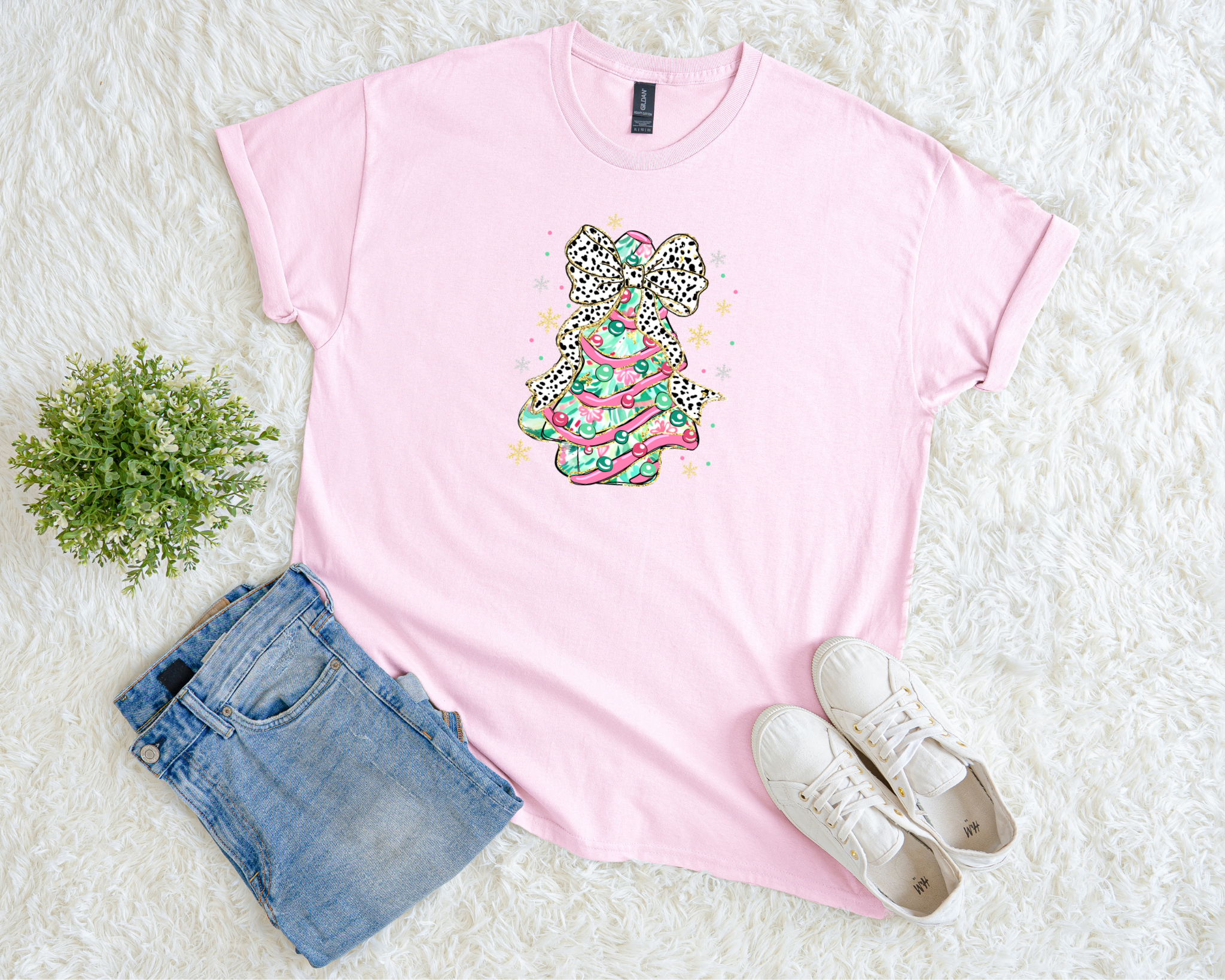 pink Christmas t-shirt featuring a colorful pink and mint tree topped with a leopard bow, styled flat with jeans and sneakers on a soft white background.